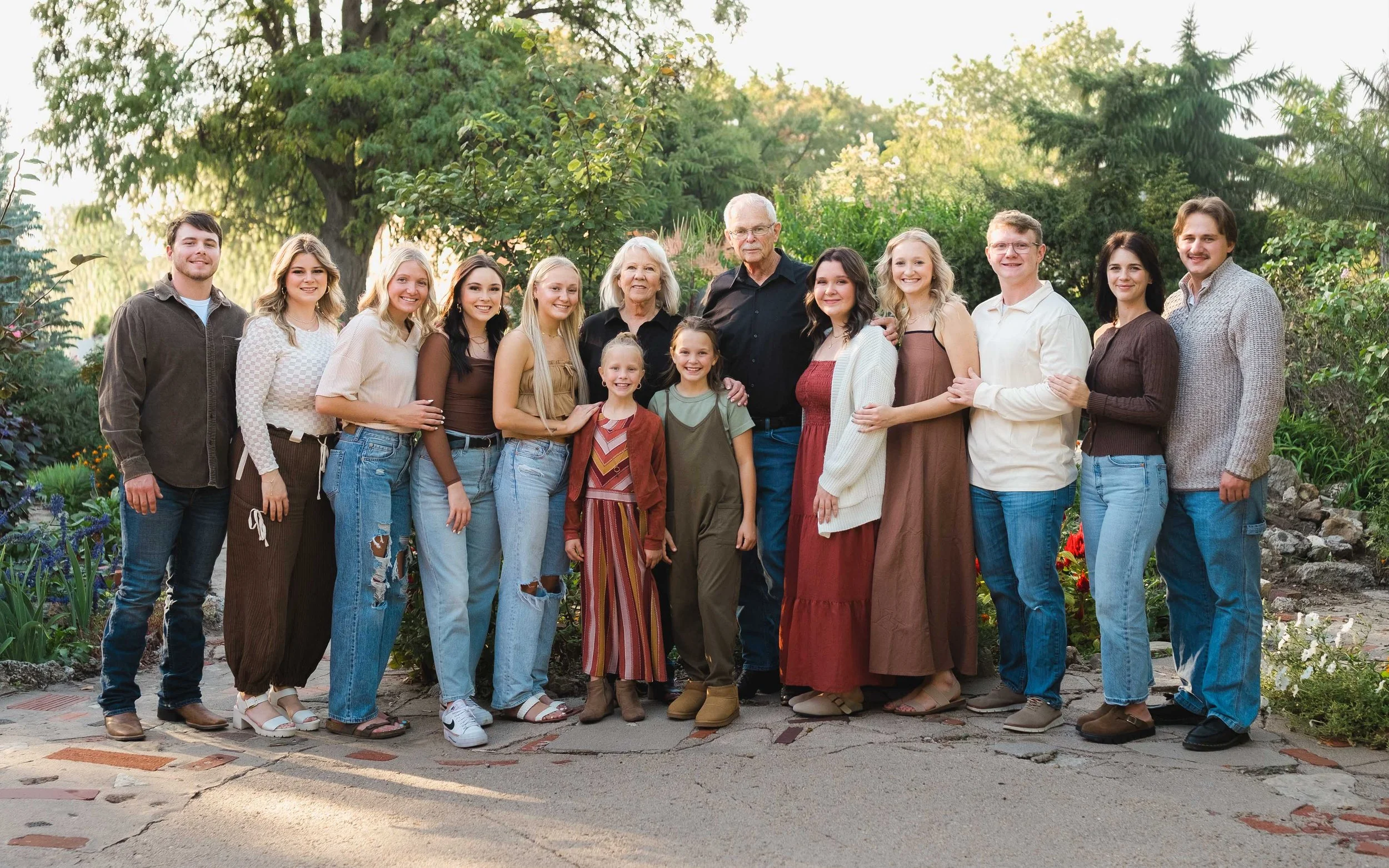 A large family group standing outdoors in a garden, with trees and bushes in the background. The family members are smiling and standing closely together.