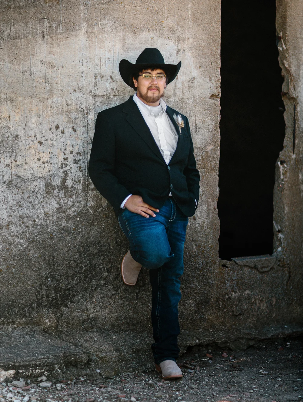 Groom in a cowboy hat leaning against a concrete wall