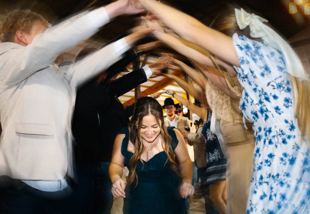 A woman walking through a tunnel of raised hands at a reception