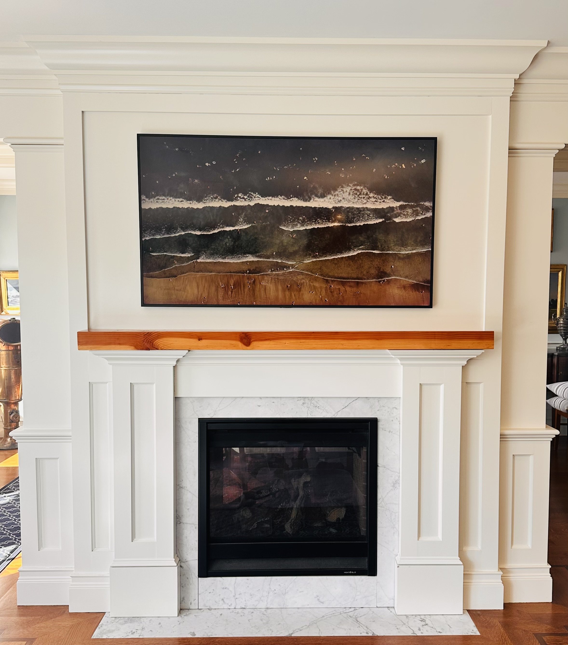 Living room fireplace with white mantel and a framed picture of ocean waves hanging above.
