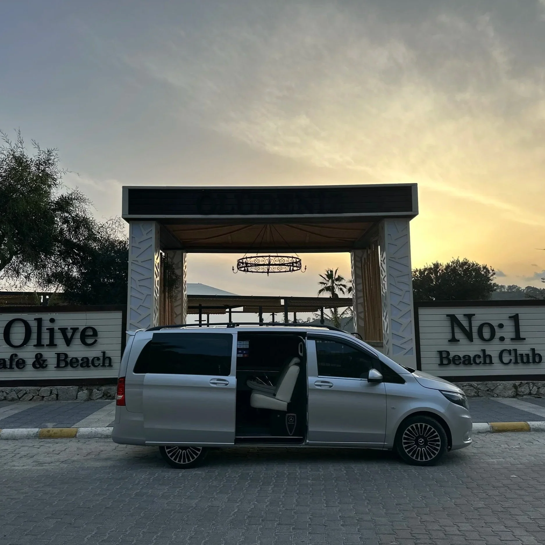 A silver minivan parked in front of the Olive Beach Club entrance at sunset.