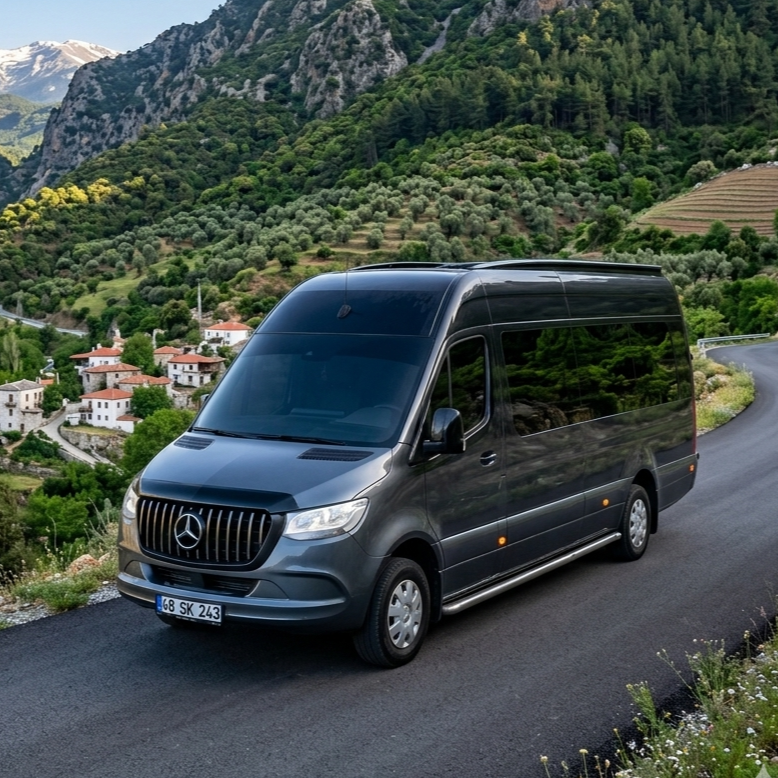 A black Mercedes-Benz van parked on a mountain road overlooking a hillside village with white houses and terraced fields, surrounded by lush green trees and steep rocky mountains.