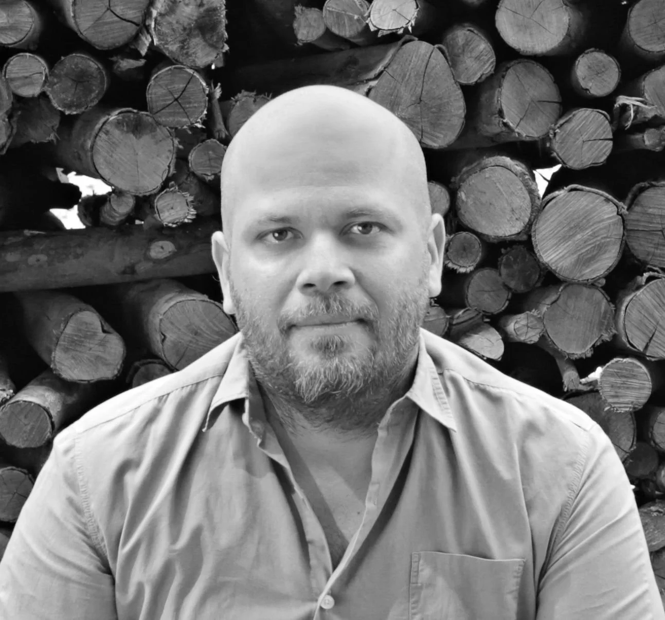 Black and white photo of a man in front of stacked logs.