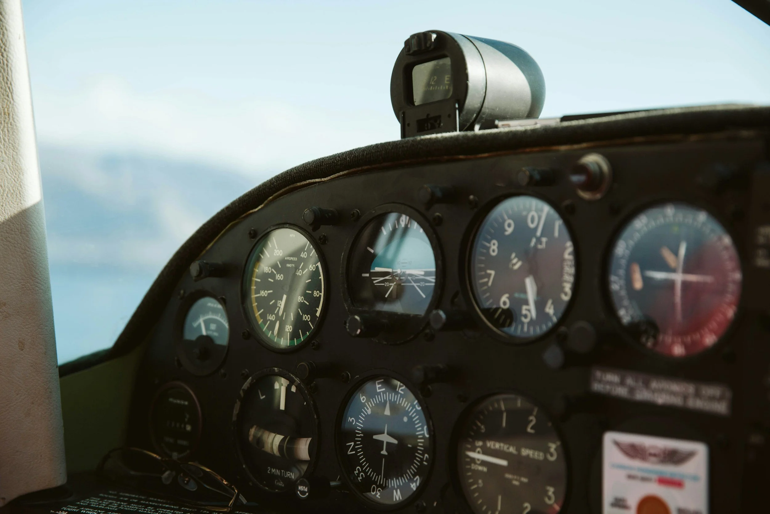 Cockpit of an airplane with multiple gauges and instruments, including altitude, airspeed, and vertical speed indicators, with a view of the sky outside the window.
