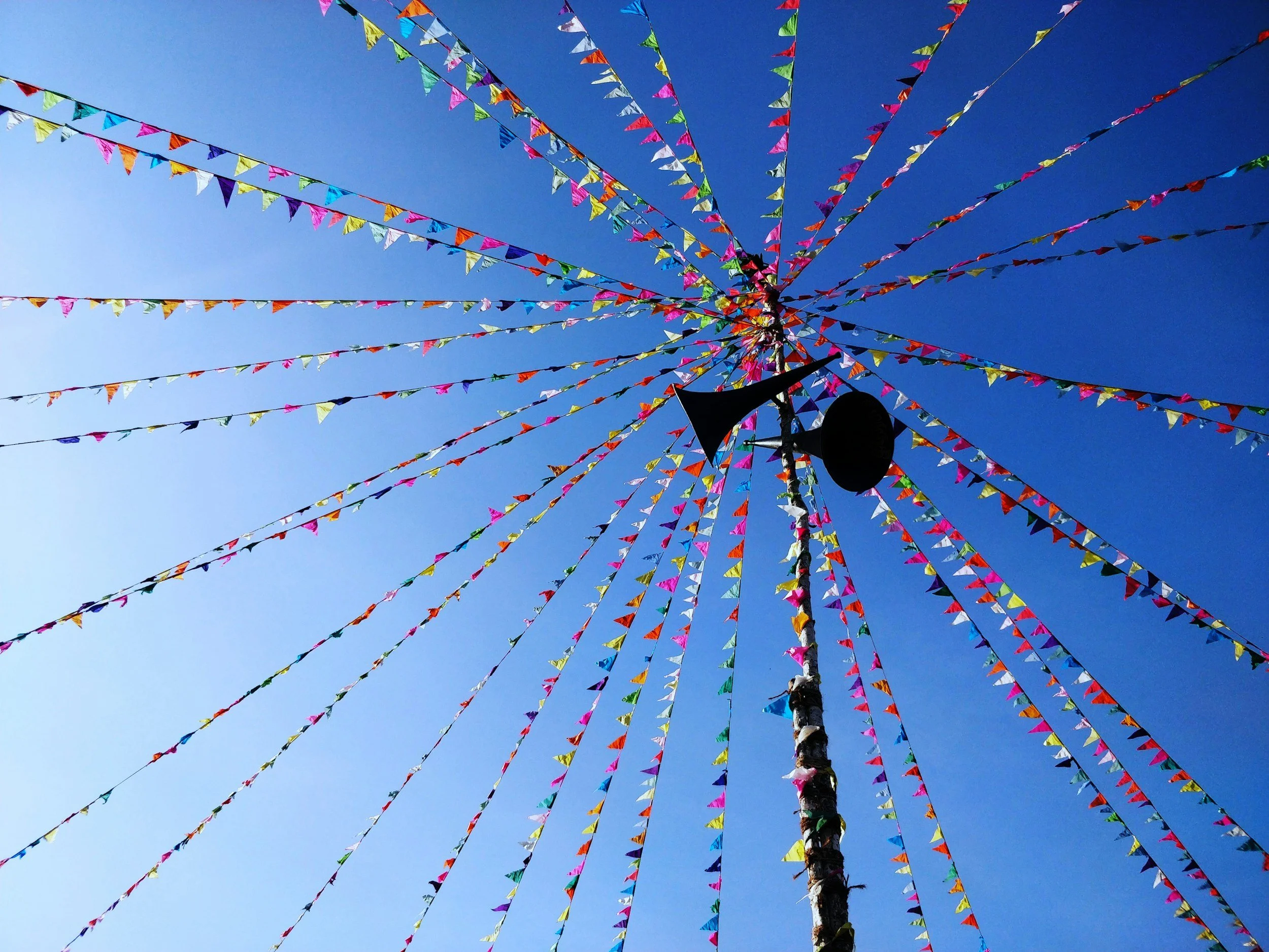 Colorful triangular flags on strings radiating outward from a central pole against a clear blue sky.