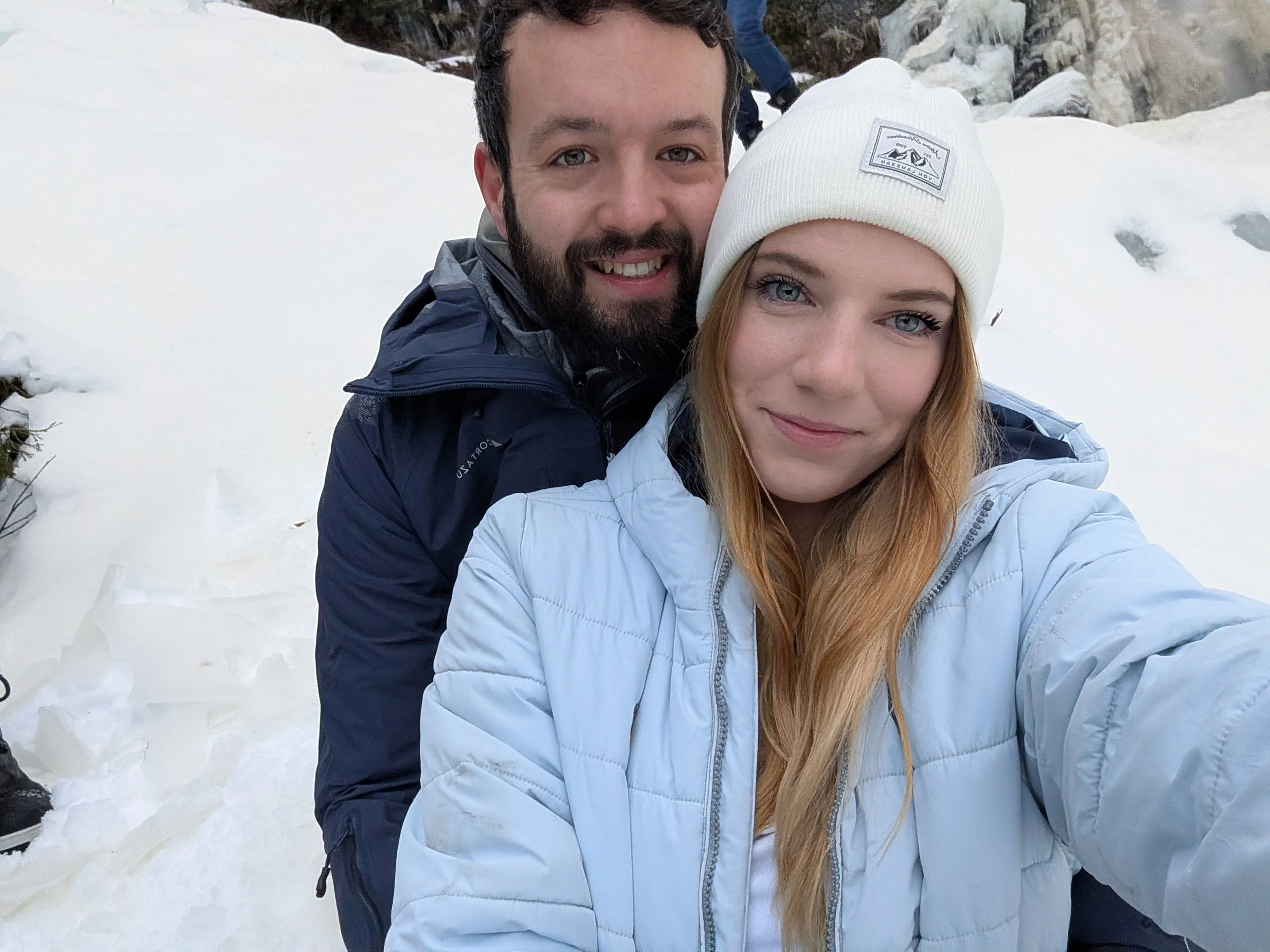 A smiling man and woman taking a selfie in a snowy outdoor setting.