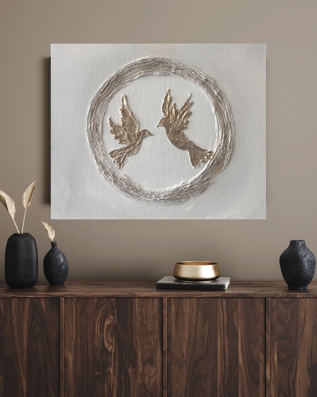 Decorative wall art featuring two birds inside a circle above a wooden sideboard with vases and a gold bowl.