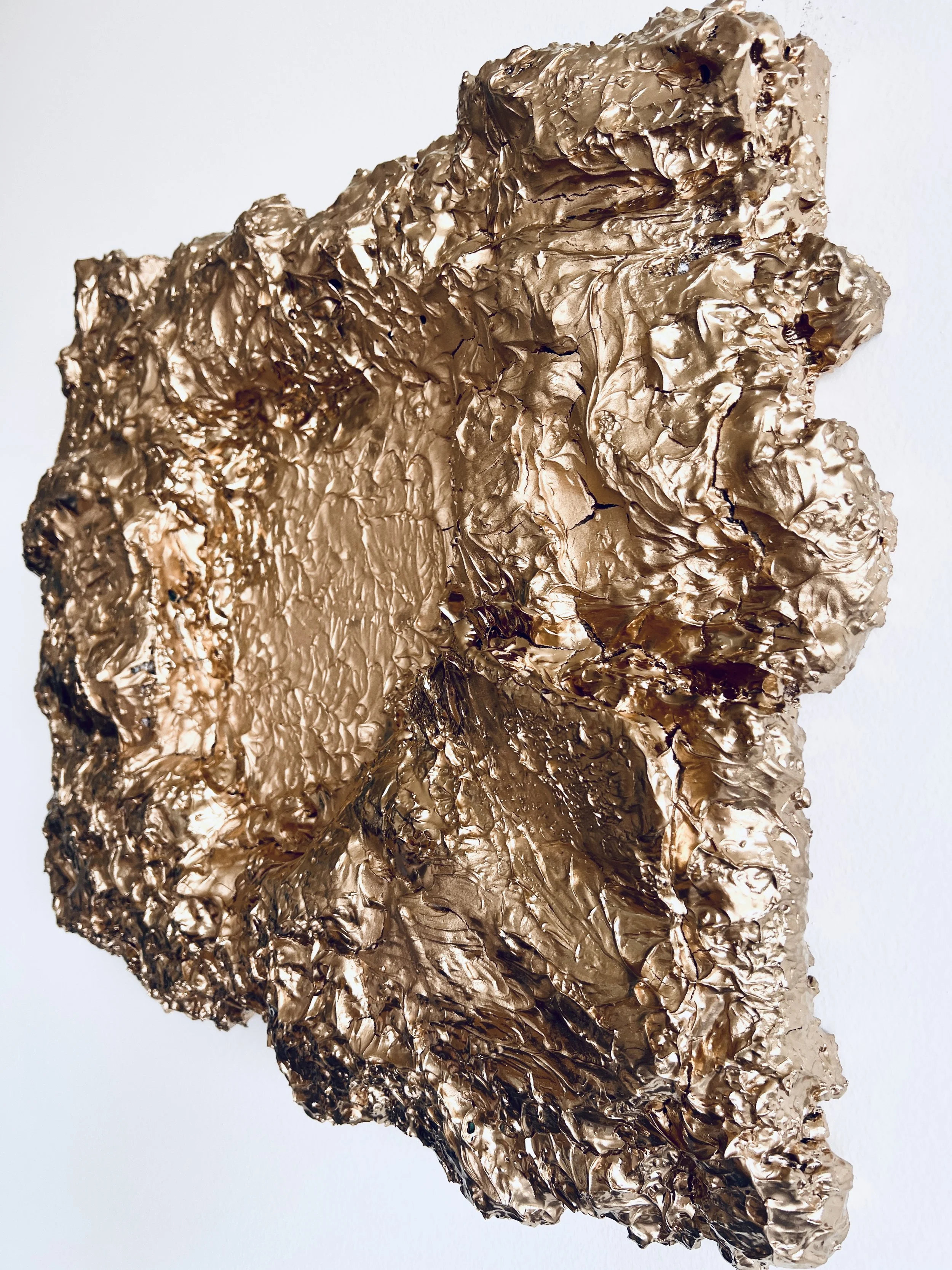 Velká, nepravidelně tvarovaná socha vytvořená z pomačkaného a vrstveného kovového materiálu v zlaté nebo bronzové barvě, umístěná na jednoduchém bílém pozadí, ve stylu fine art. Ideální pro milovníky moderního umění, abstraktních a texturovaných reli