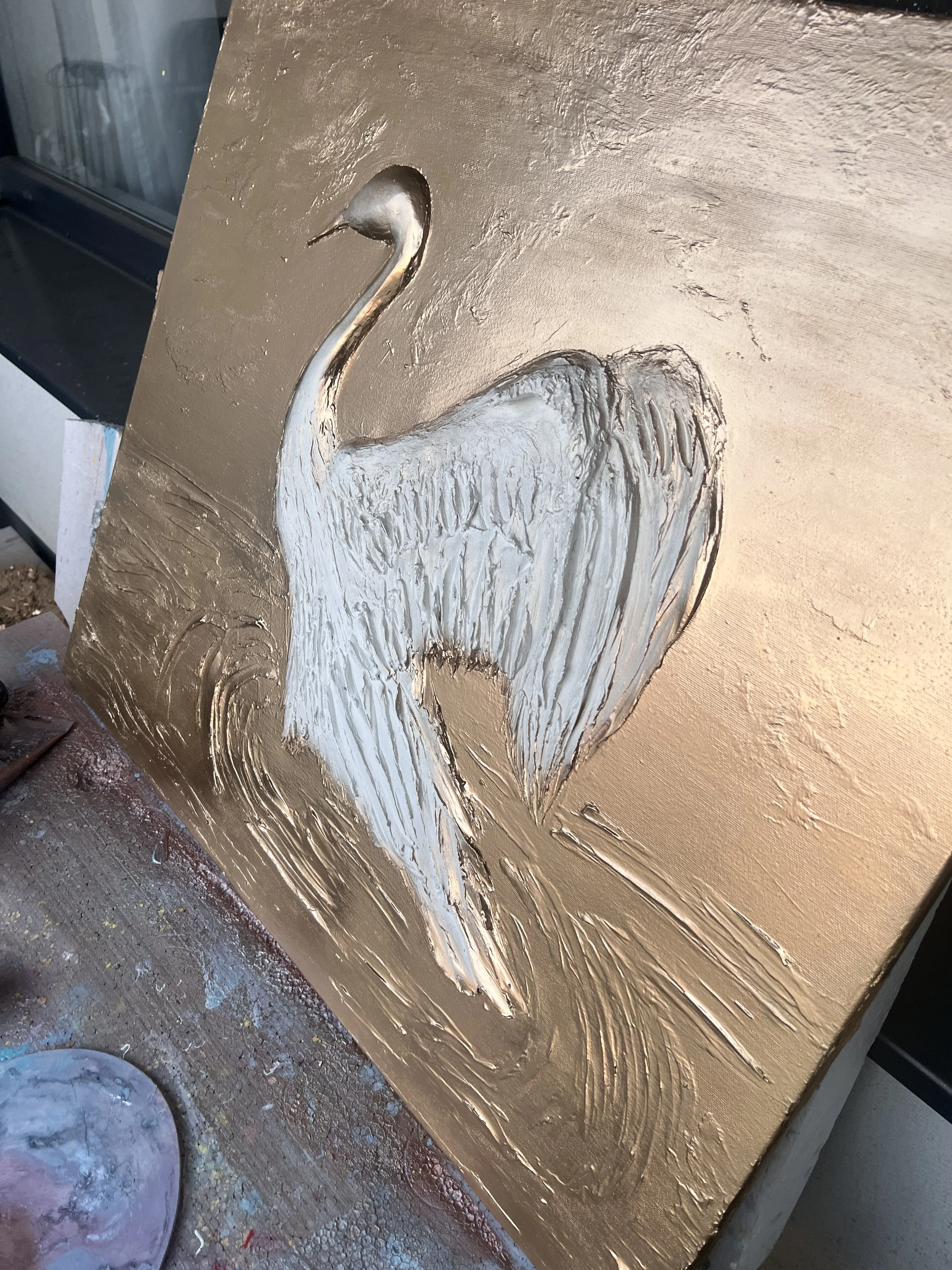 A painting of a white heron with a long neck, standing on water, on a gold background.