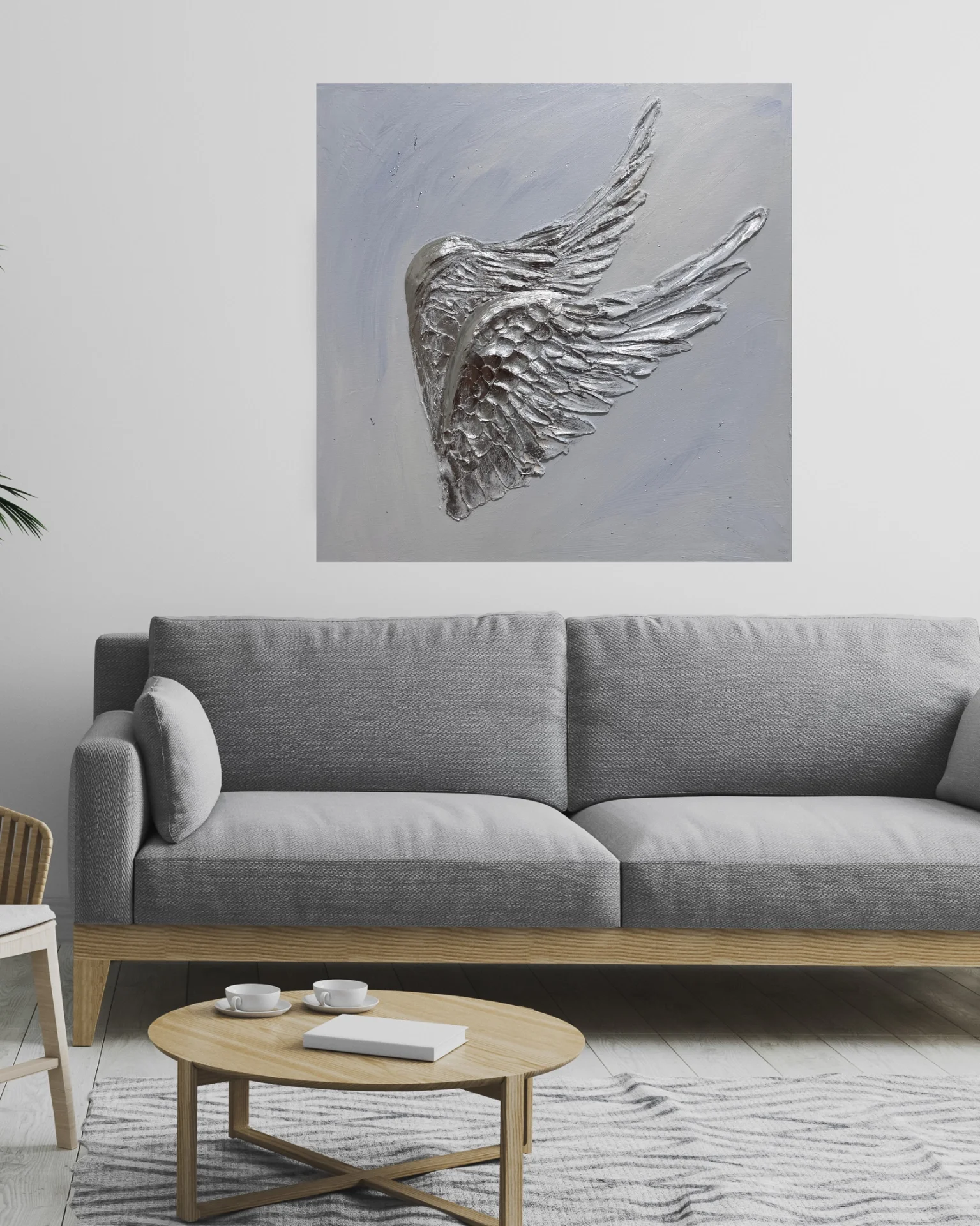Silver decorative wall art of a winged bird's head hanging above a gray sofa in a modern living room.