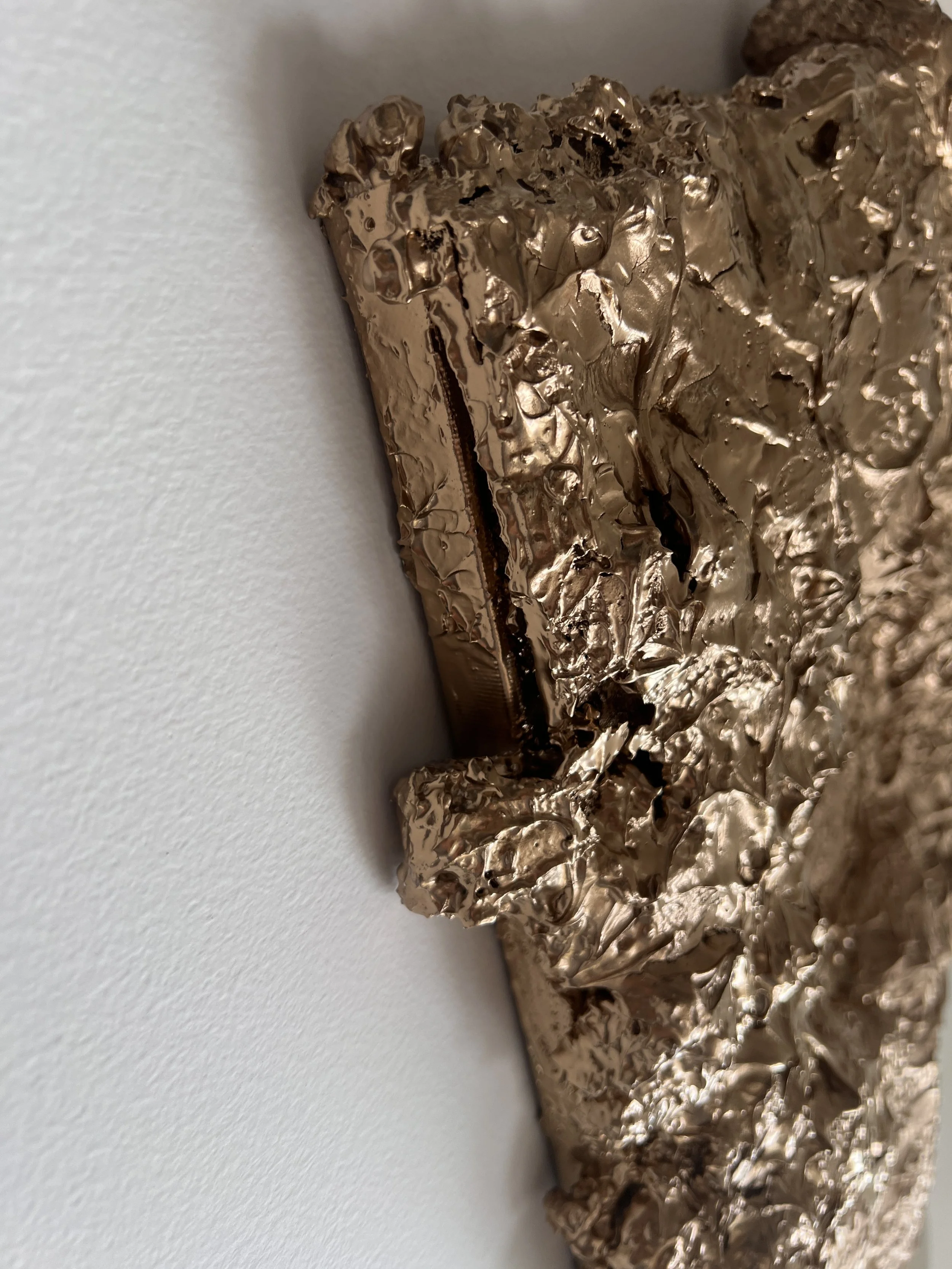 Pomačkaná zlatá fólie na bílém povrchu s viditelnou malou zipovou sekcí, ve stylu fine art. Ideální pro milovníky moderního umění, texturovaných a abstraktních reliéfních děl.