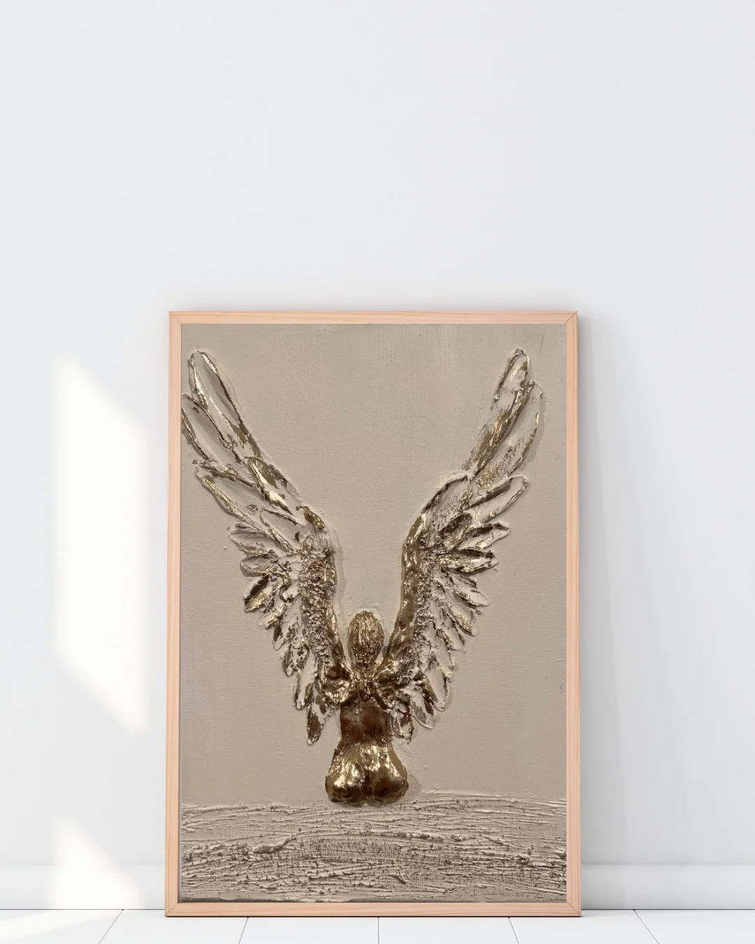 Framed artwork featuring a metallic sculpture of a bird with outstretched wings, mounted on a wooden frame and leaning against a white wall.