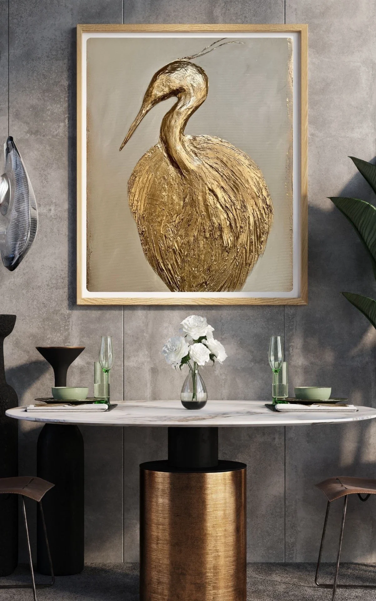 A modern dining room with a marble table, white flowers in a glass vase, two glasses, and tableware, with a large framed painting of a golden heron on the wall behind.