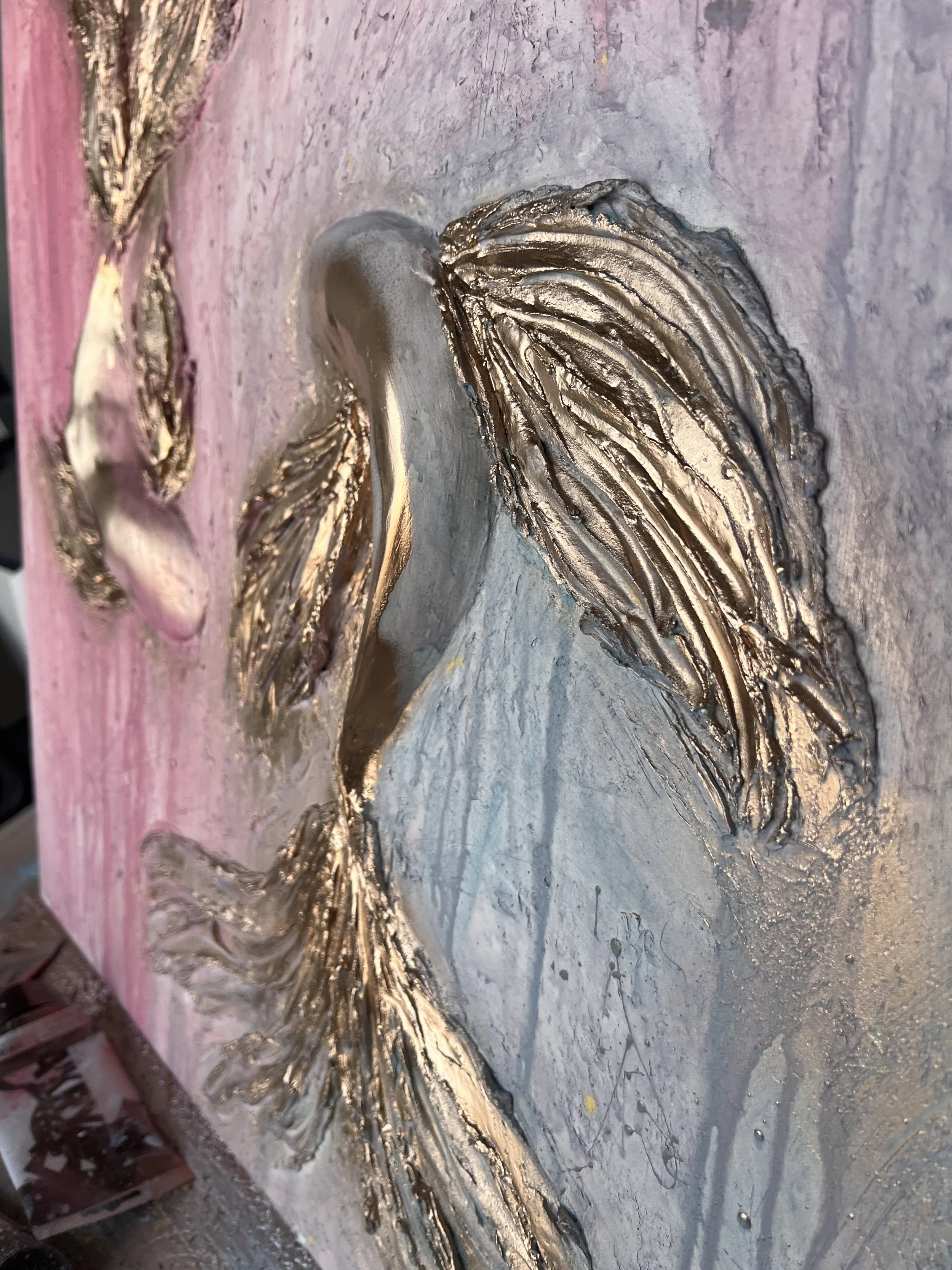 Close-up of a textured, metallic whale sculpture with gold and silver accents, mounted on a pink and white background.