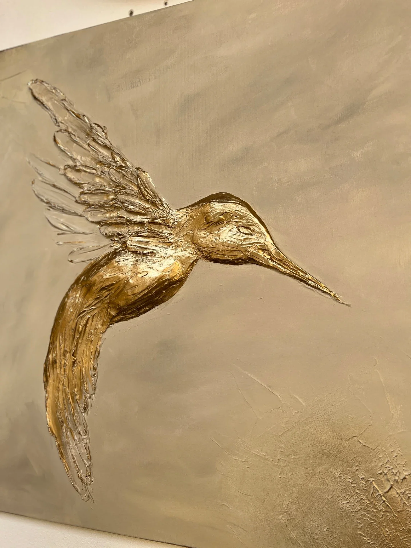 A golden textured painting of a flying hummingbird with wings spread.