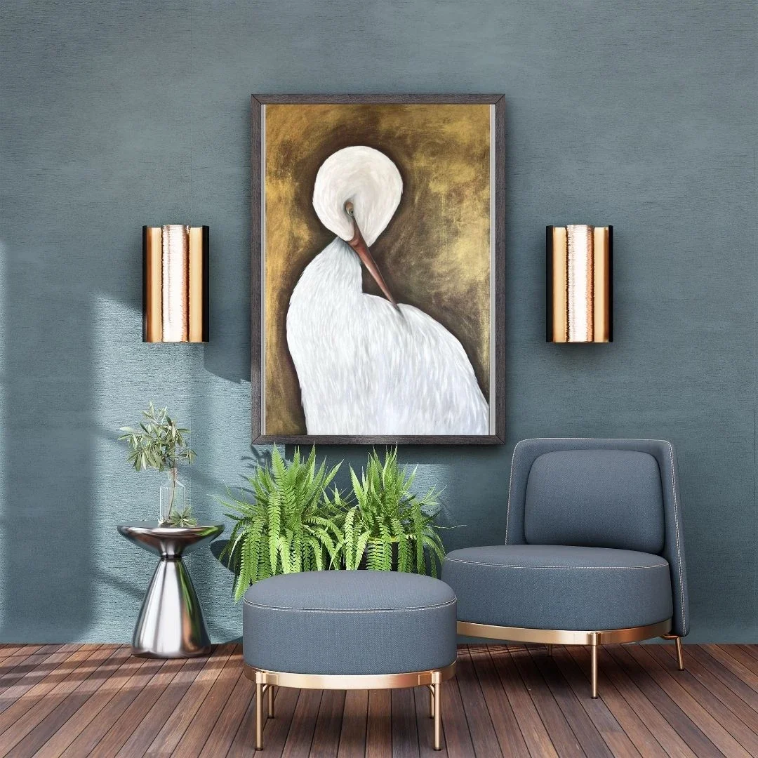 A cozy living room corner with a blue armchair and matching ottoman, a large framed painting of a white swan on the blue wall, two gold wall sconces on either side, a small metal side table with a potted plant, and green plants on the floor.