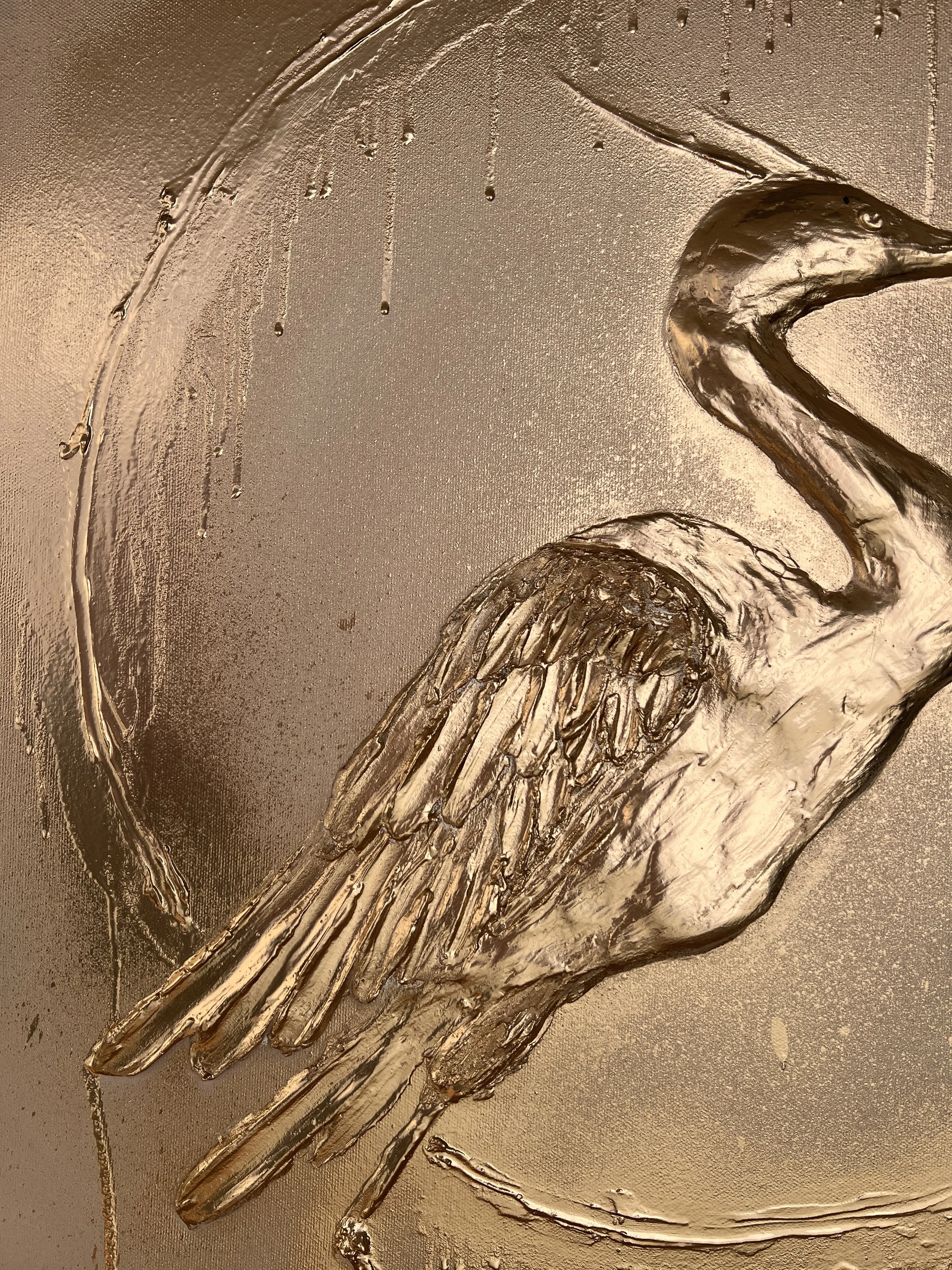A metallic or bronze-colored embossed or textured art piece of a heron or crane bird, showing its profile with a long neck, beak, and detailed wing feathers.