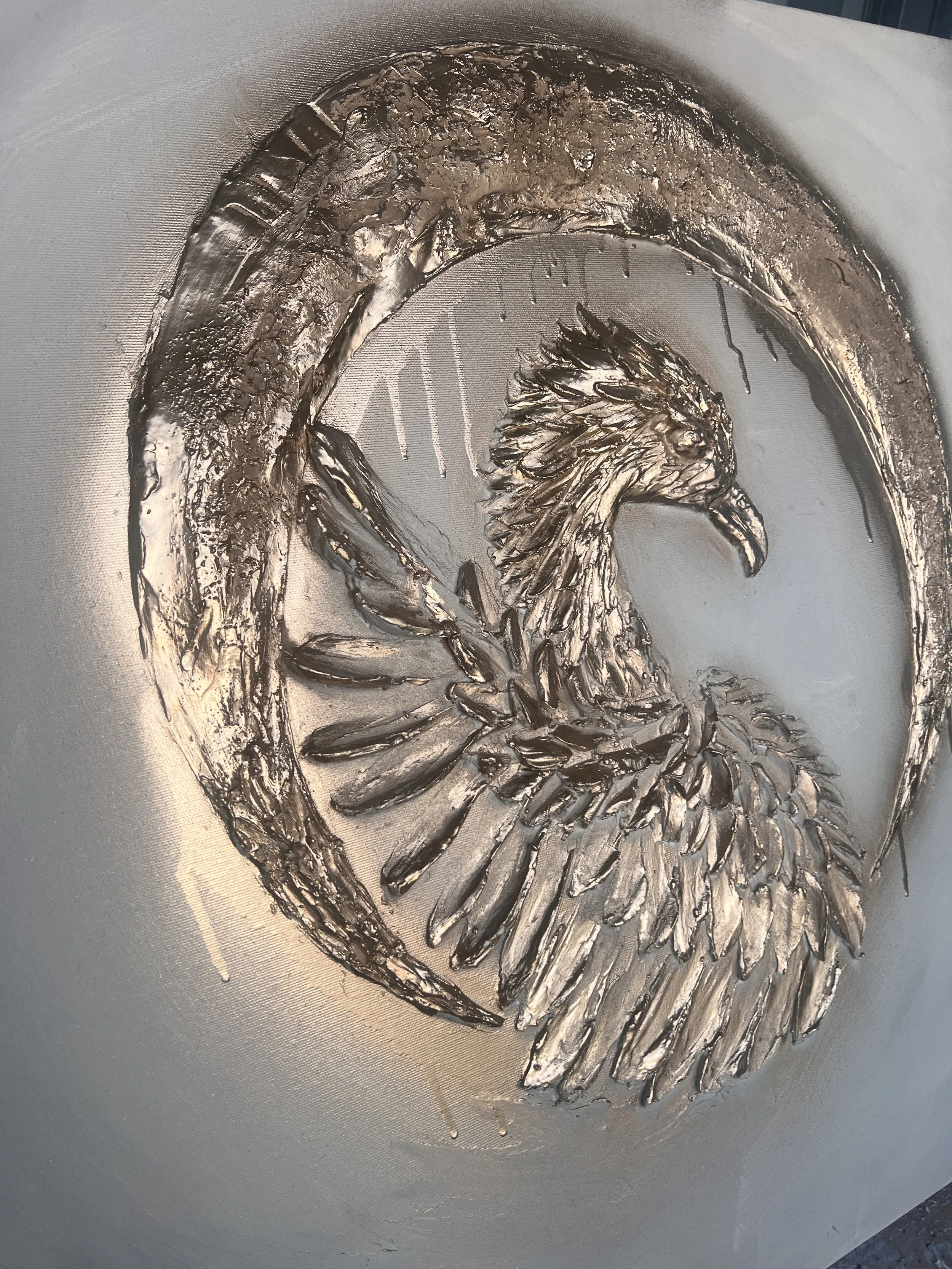 Metalová reliéfní socha fénixe s detailně propracovaným peřím, obklopená polokruhovou páskou, ve stylu fine art. Ideální pro milovníky moderního umění, sochařských a texturovaných reliéfních děl.
