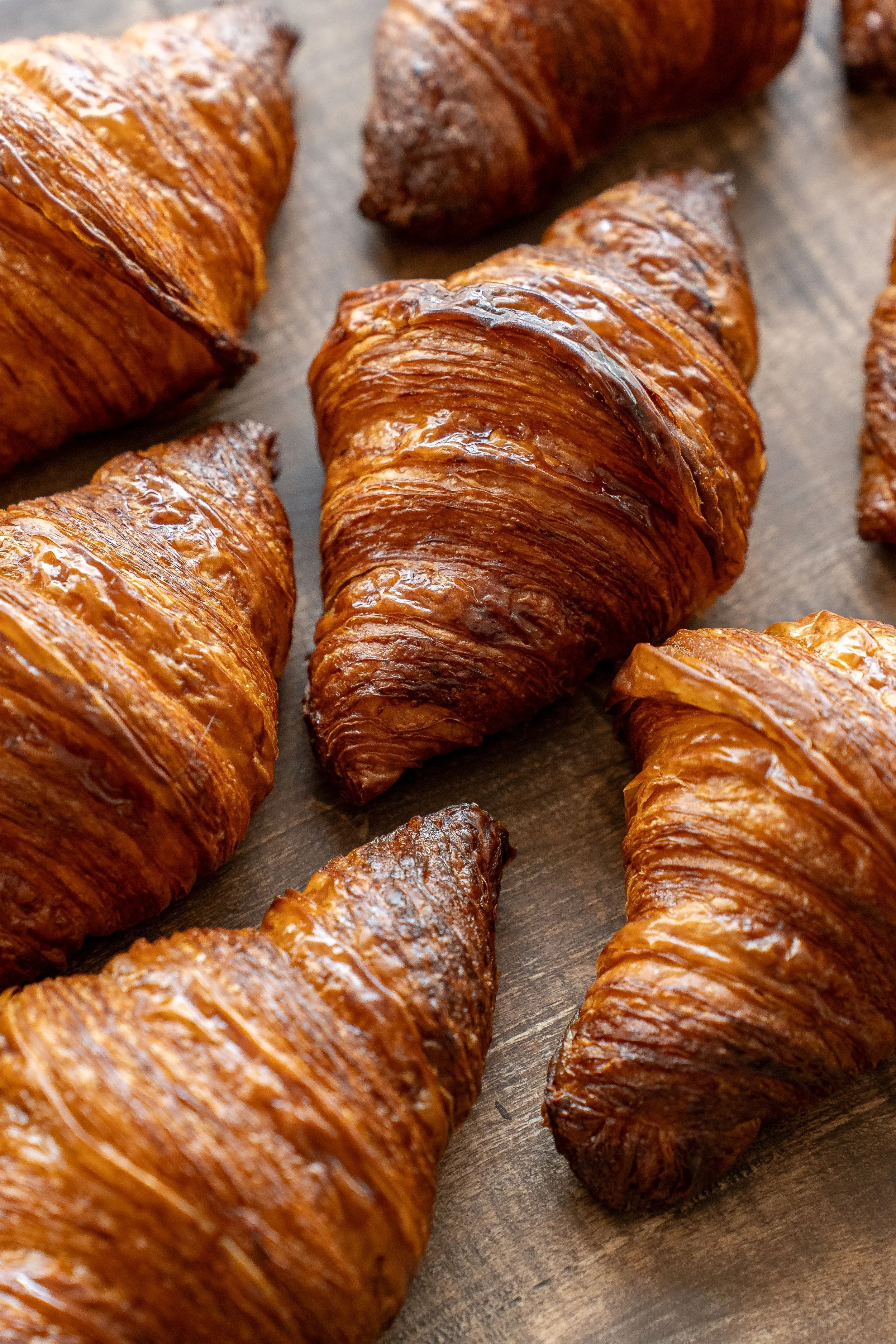 Close-up image of several freshly baked croissants on a wooden surface.