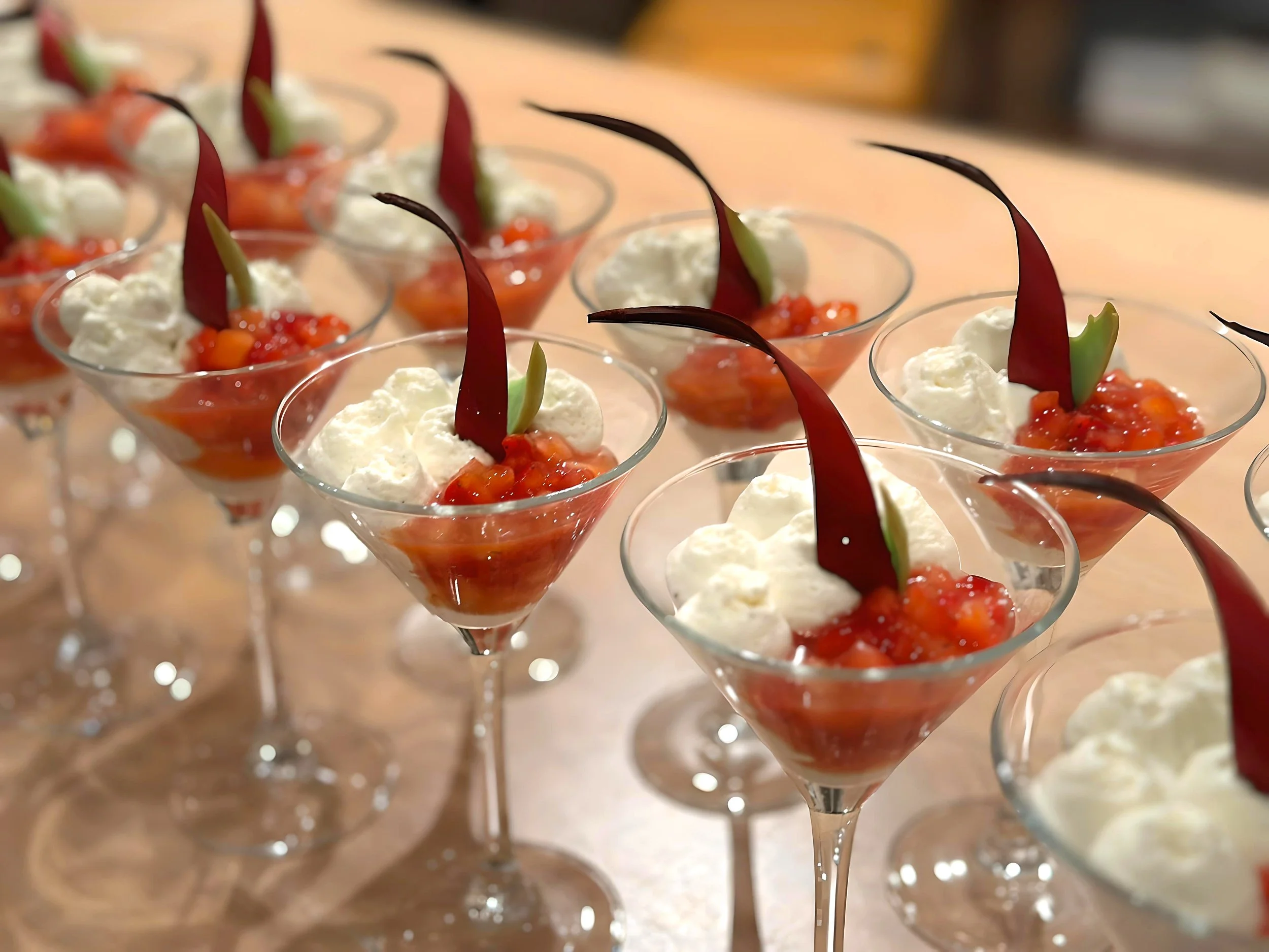 Kleine Speisen in Gläsern mit roter Basis, weißer Creme und dunkelroter Garnitur.