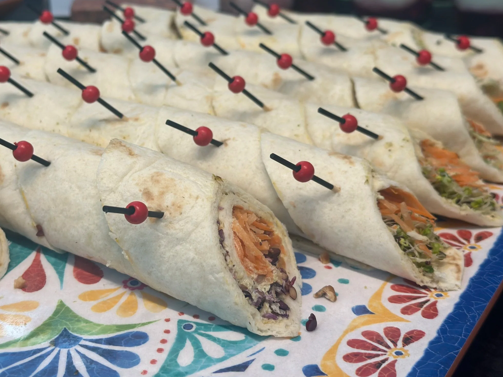 Gefüllte Wrap-Häppchen mit kleinen Spießen auf einer gemusterten Platte.