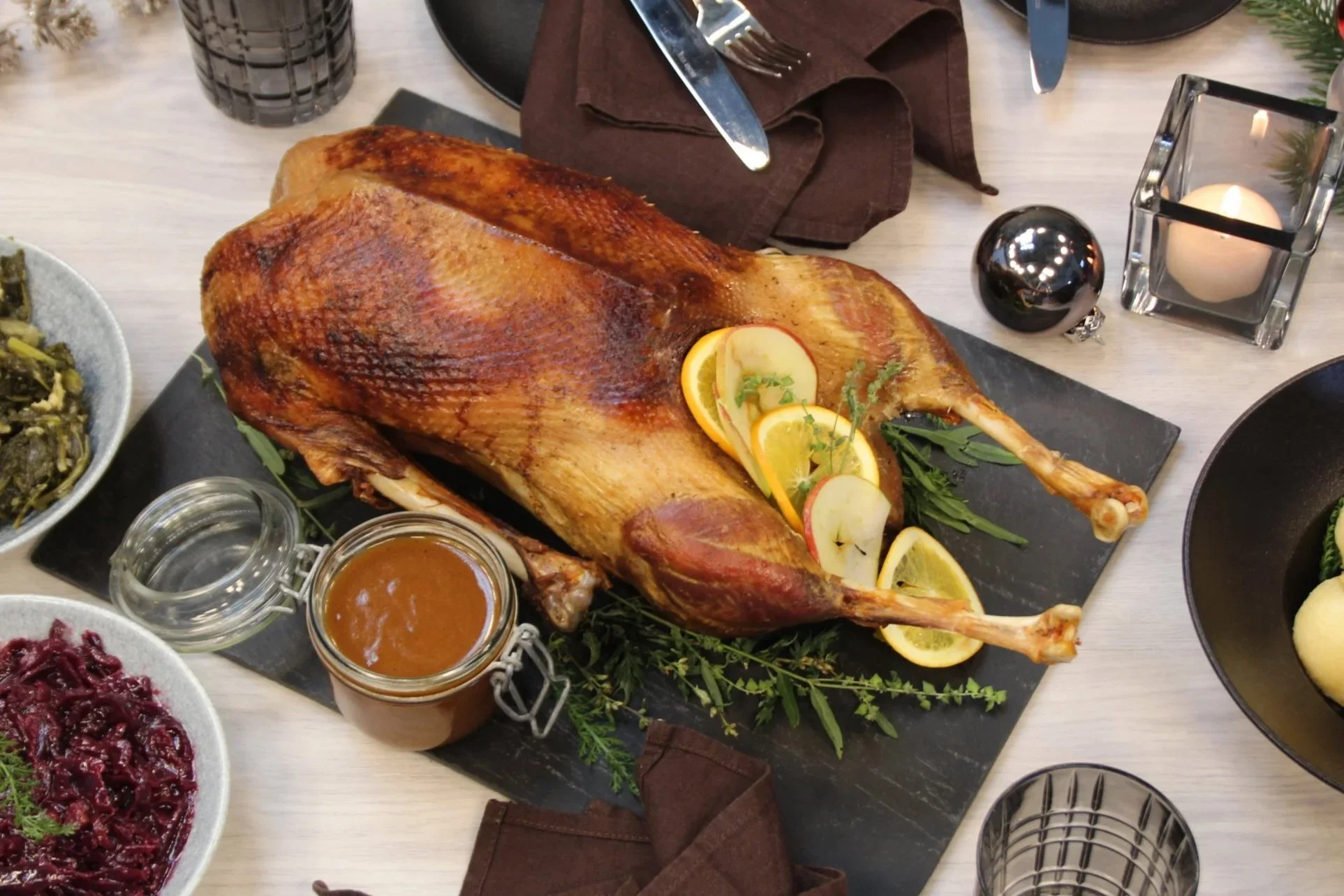 Weihnachtsgänsebraten mit Orangenscheiben, Kräutern und Beilagen auf einer festlich gedeckten Tafel. Zum Weihnachtscatering-Angebot.