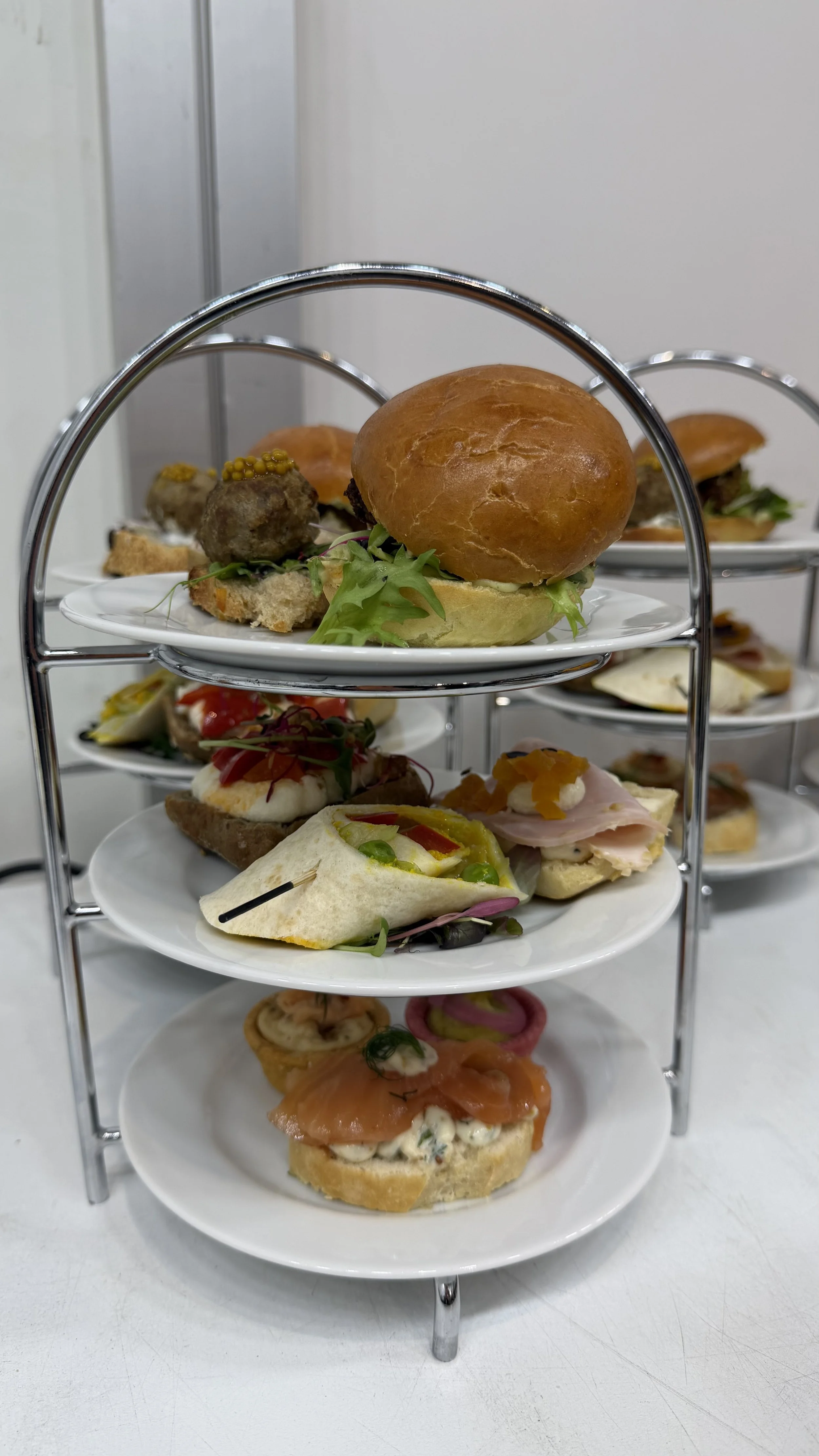 Etagere mit Petits, einem Burger, belegten Brötchen und weiteren kleinen Speisen.