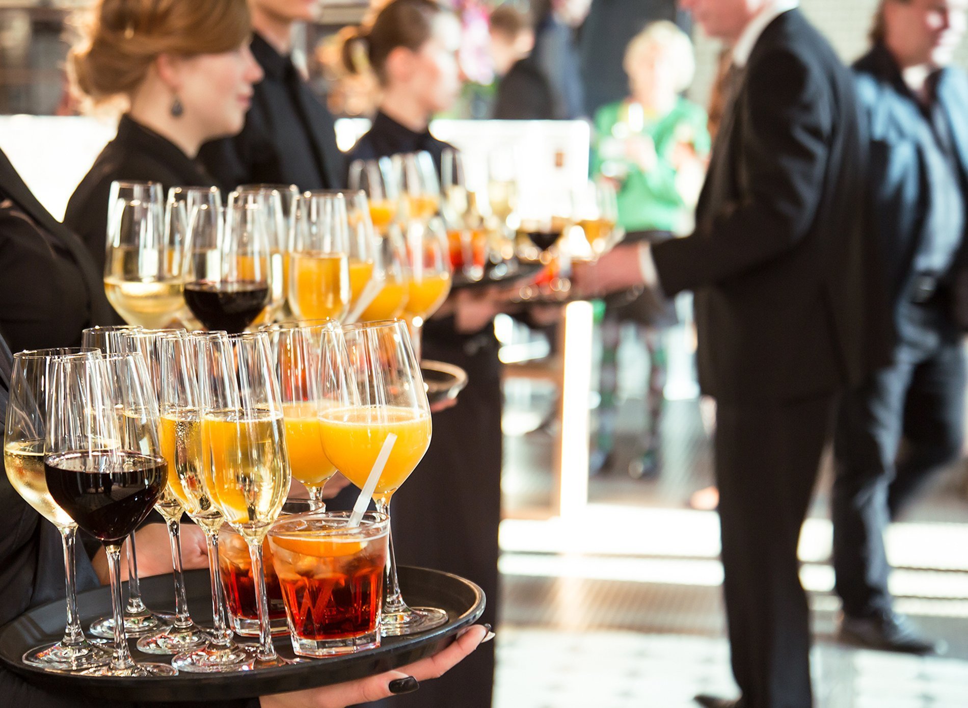Servicemitarbeitende halten Tabletts mit Wein, Sekt und weiteren Getränken für die Gäste bereit.
