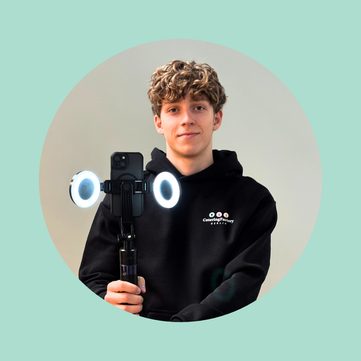 Junge mit dunklem Hoodie, der einen Smartphone-Stabilisator mit Ringlichtern hält.