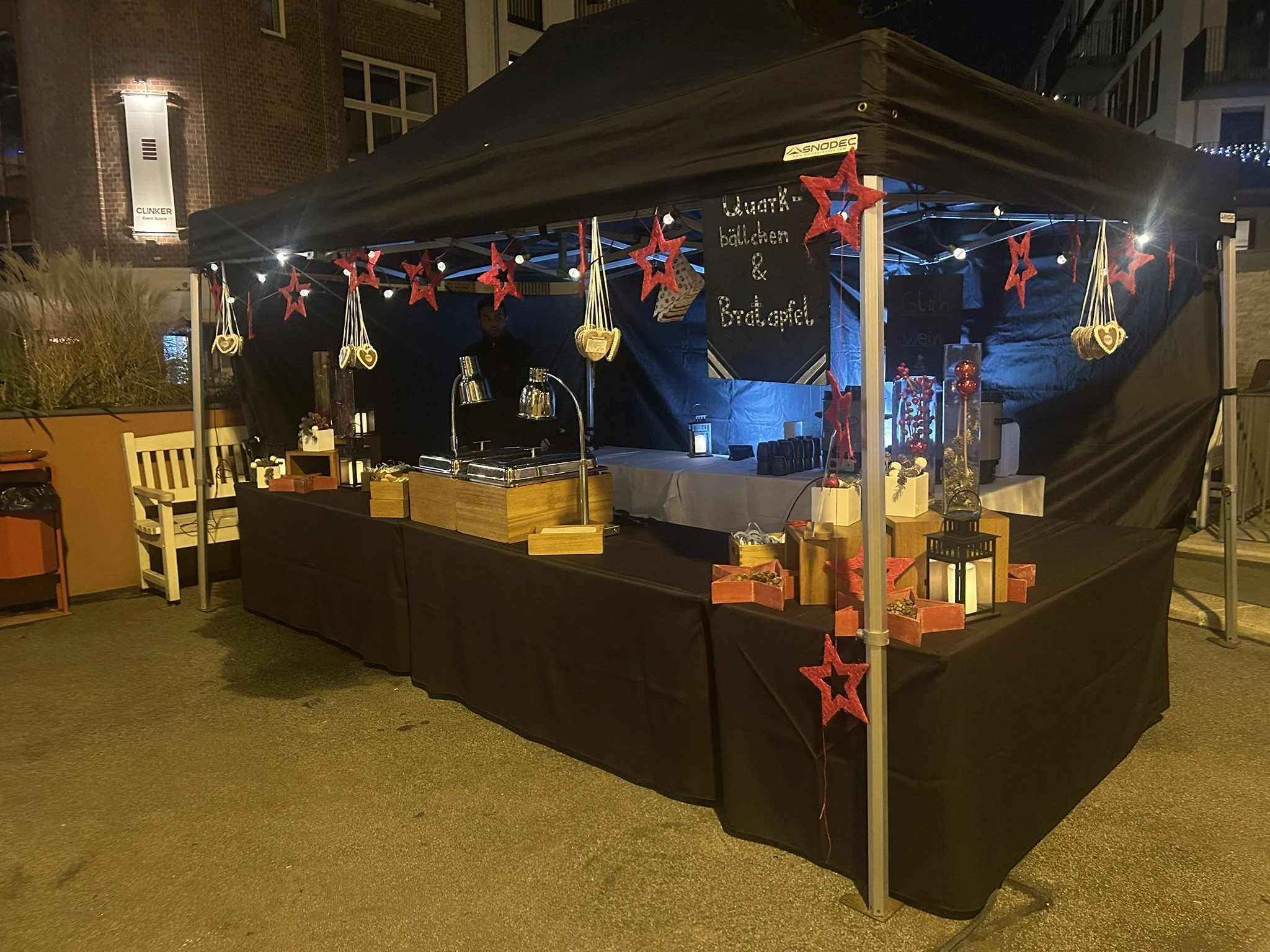 Weihnachtsmarktstand unter einem schwarzen Pavillon, geschmückt mit roten Sternen und einer Lichterkette.