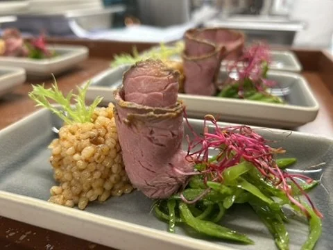 Aufgeschnittenes Fleisch mit goldbrauner Graupen-Beilage, Blattsalat und roten Sprossen auf rechteckigen Tellern.
