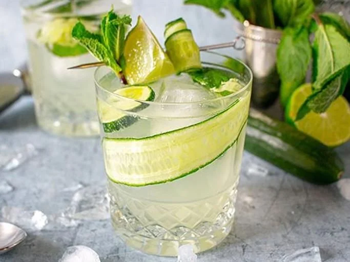 Helle Drinks mit Eis, Gurkenstreifen, Limettenspalten und Minze.