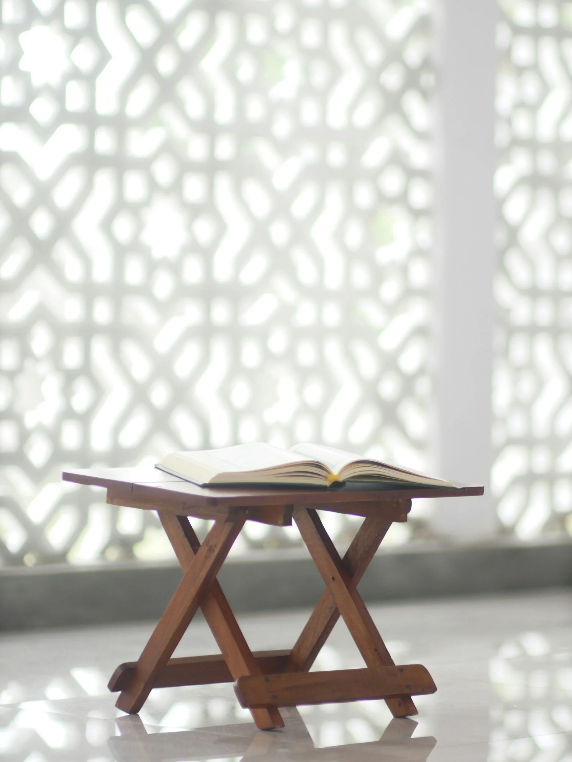 Open book on a small wooden stand in front of a decorative white lattice window.