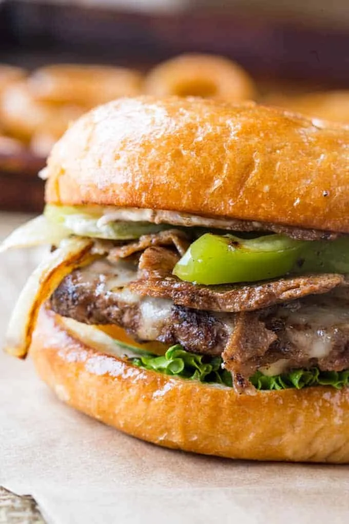 Close-up of a cheeseburger with grilled beef patty, lettuce, pickles, cheese, onions, and a toasted bun.