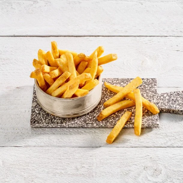 A bowl of French fries on a textured rectangular board on a white wooden surface.