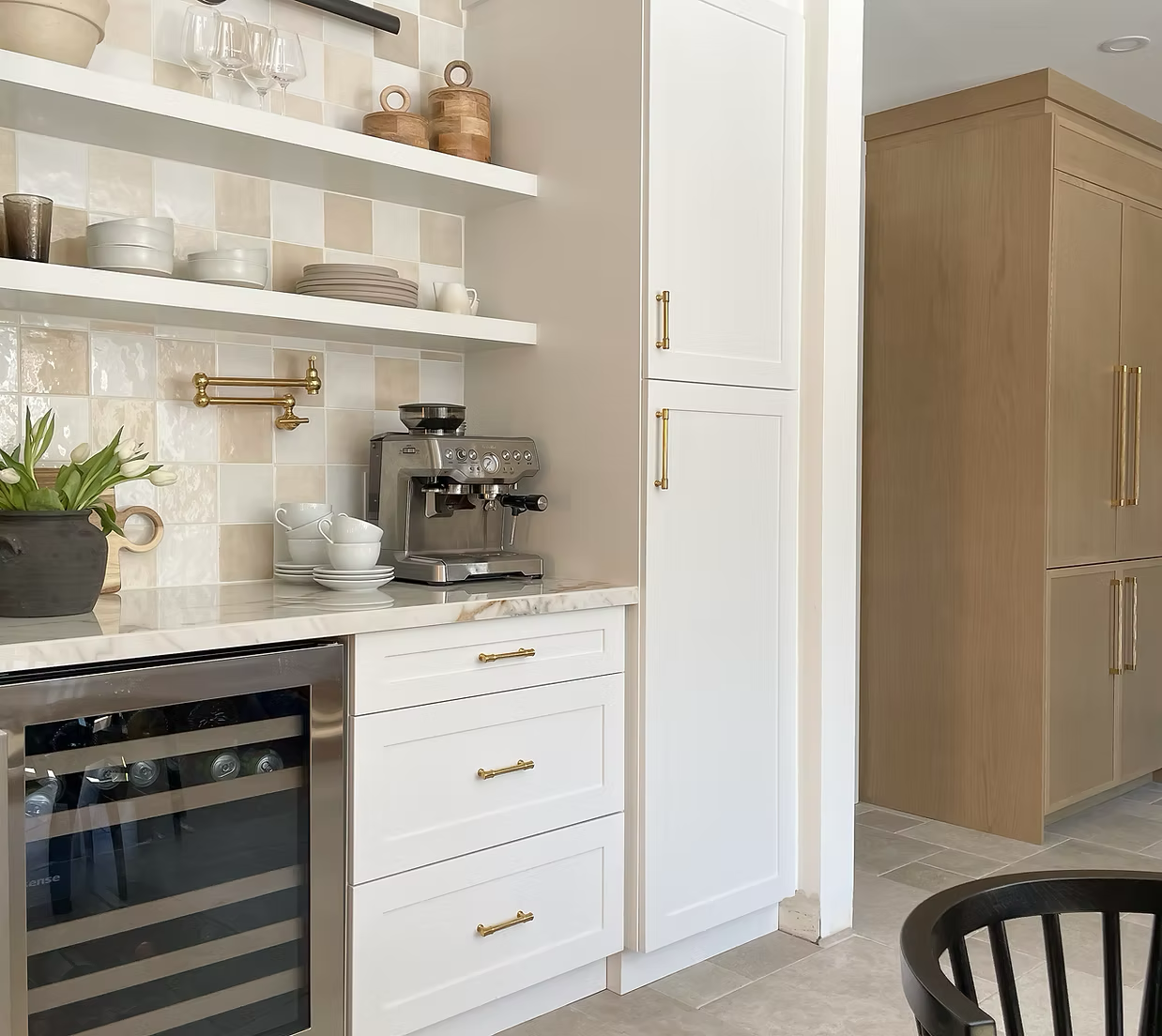 A modern kitchen corner with white and wood cabinets, beige tile backsplash, open shelves with glassware and dishes, a coffee machine, a potted plant, and a mini wine cooler.