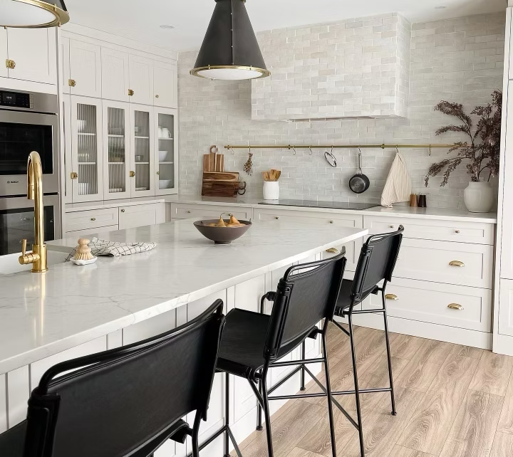 Modern kitchen with white cabinetry and marble countertops, black bar stools, gold accents, and decorative items on the counter.