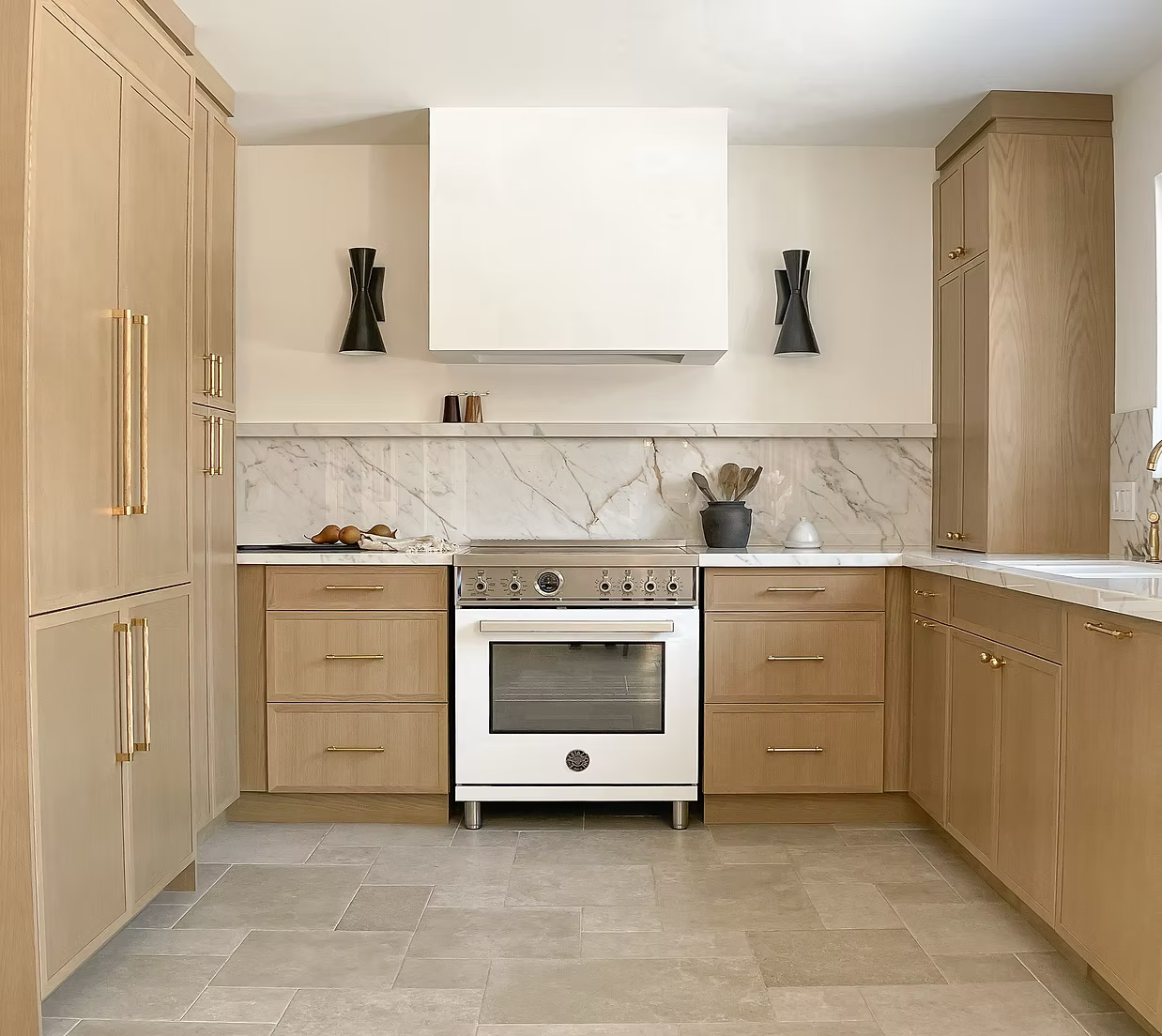 Kitchen with light wood cabinets, marble backsplash, white oven, black decor, and beige tile flooring.