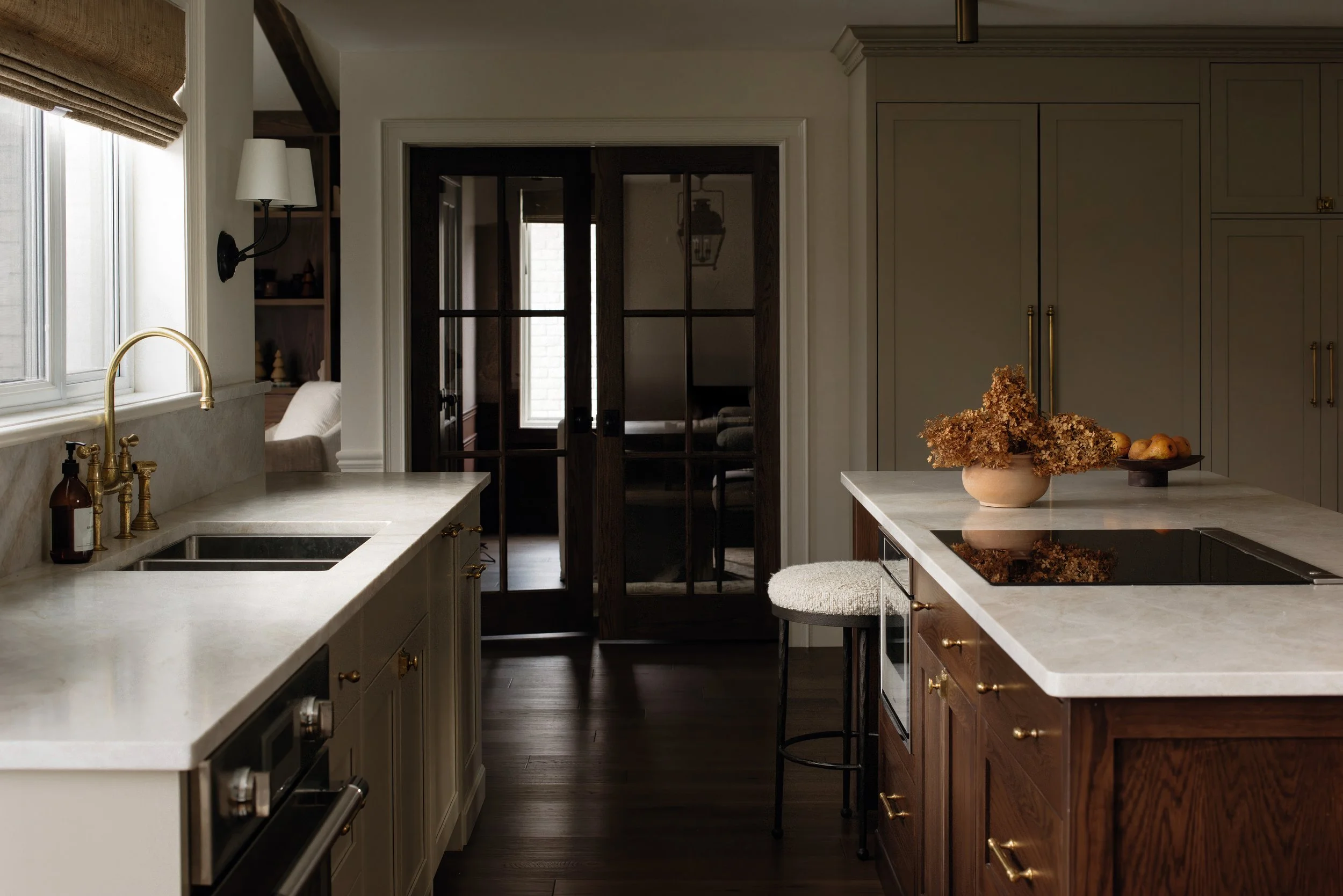 Modern kitchen with white and dark wood cabinets, marble countertops, and glass sliding doors leading to another room.