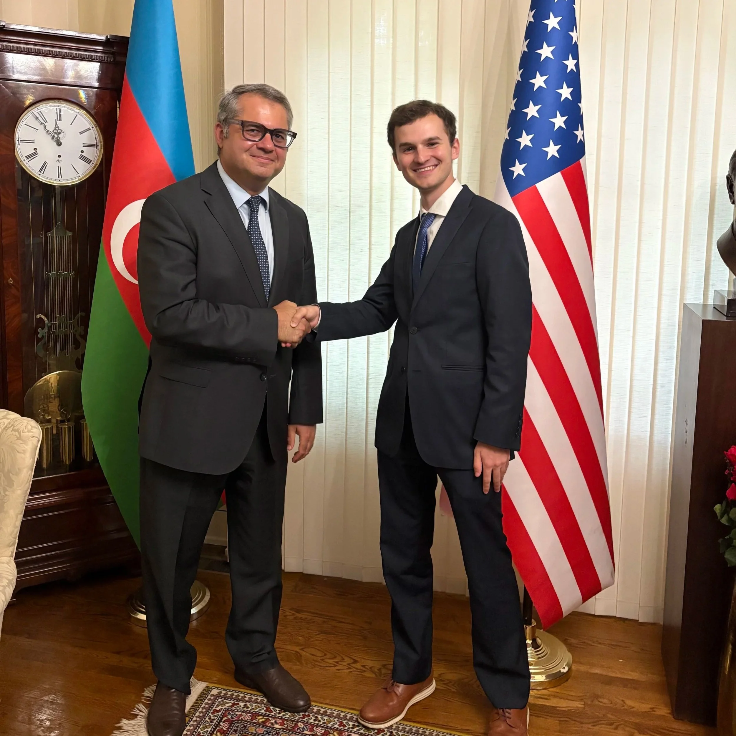 Brady Knox and Azerbaijani Ambassador Khazar Ibrahim shaking hands in a room with Azerbaijani and American flags in the background.