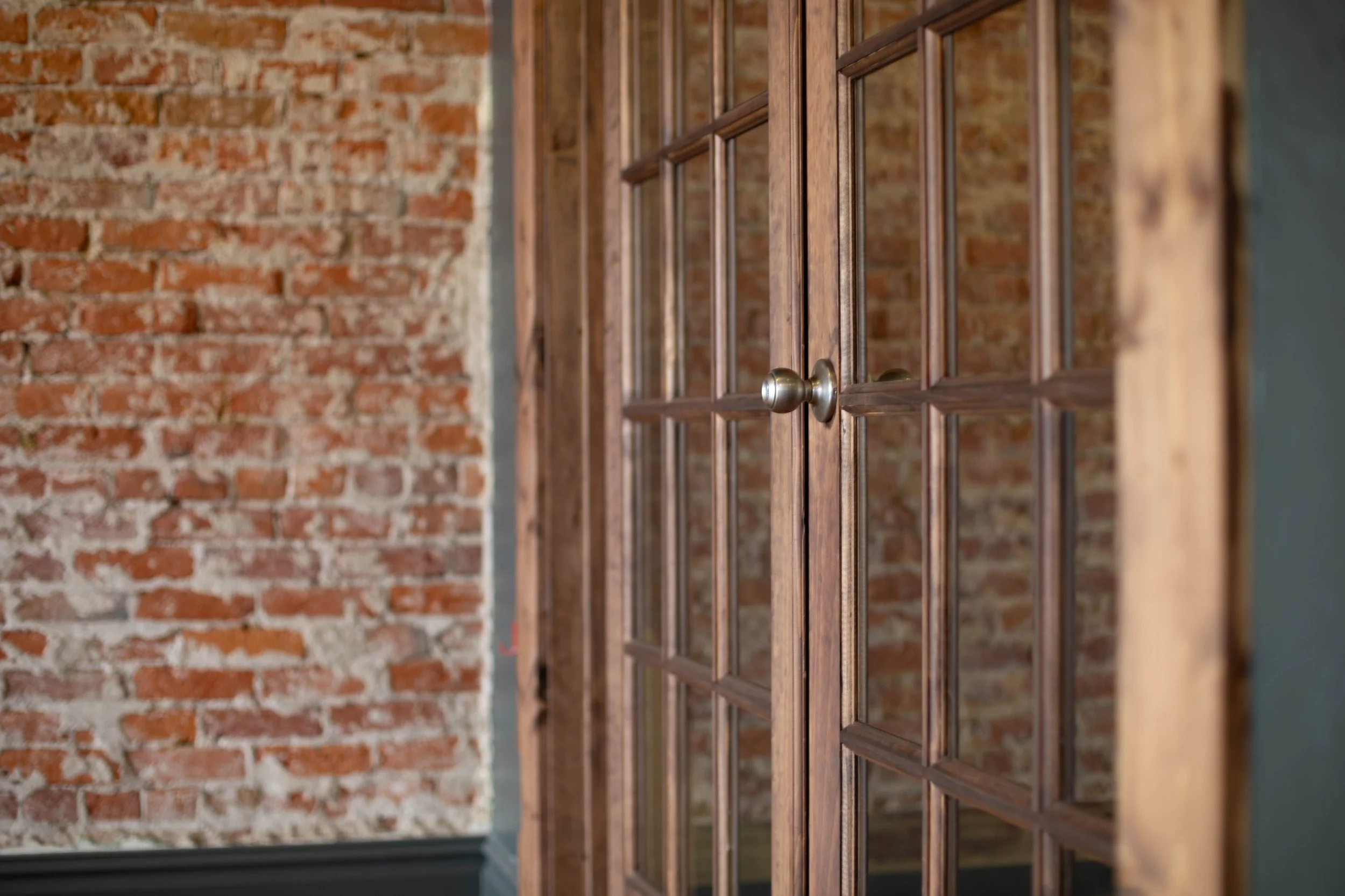 Close-up of a wooden glass-paneled door with metal doorknob, against an exposed brick wall.