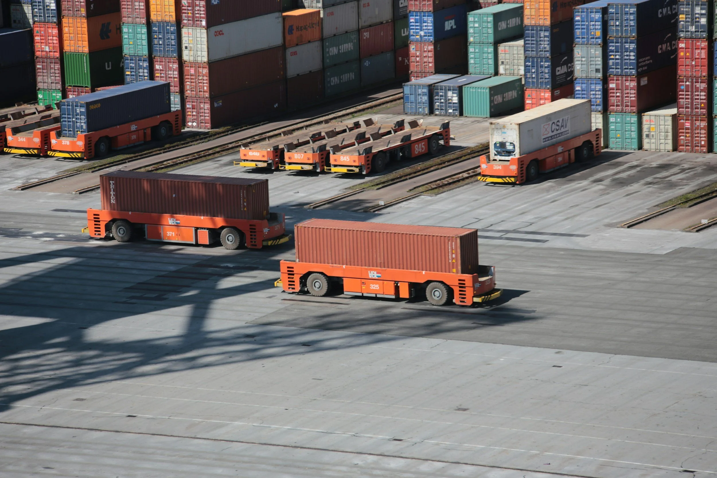 Multiple orange cargo trains with containers on tracks and concrete loading areas, surrounded by a variety of stacked shipping containers in a logistics yard.