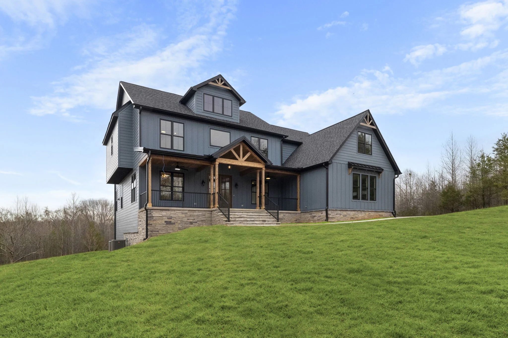A modern two-story house painted in blue with black window frames, situated on a grassy hill under a partly cloudy sky.