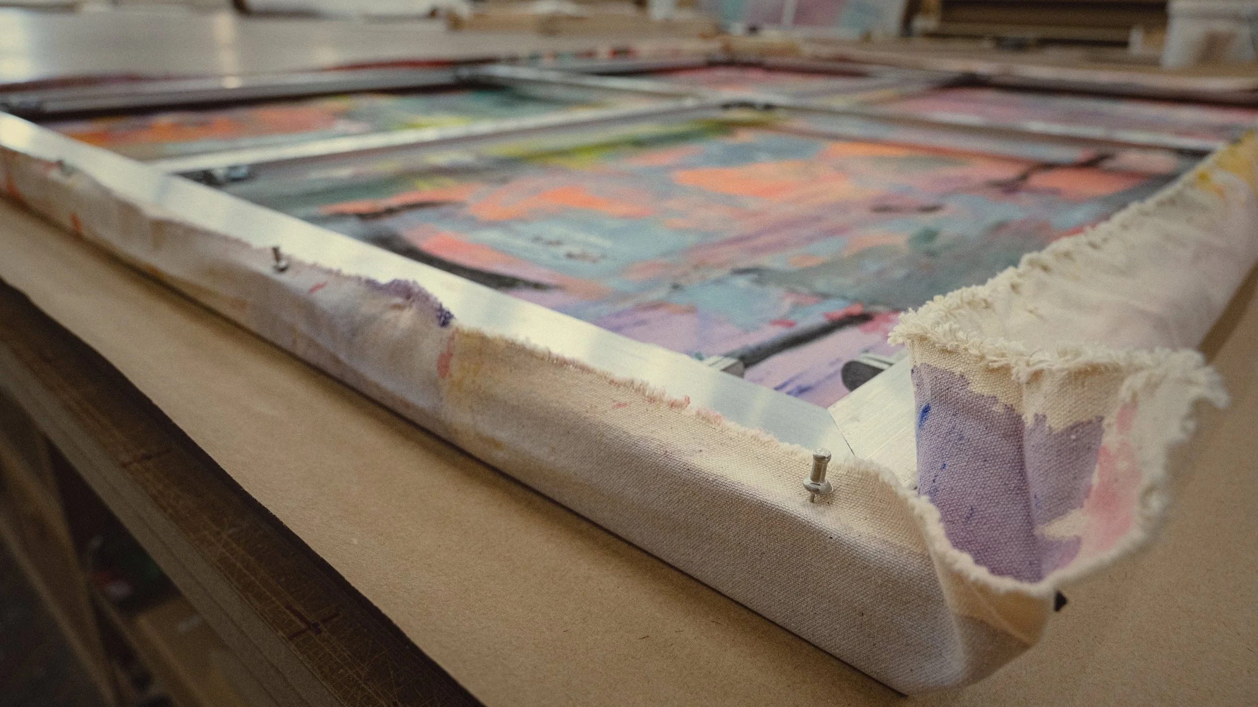 Close-up of a tacked painting being prepared, with fabric around the edges and small metal tacks securing the fabric to the frame to be stretched.