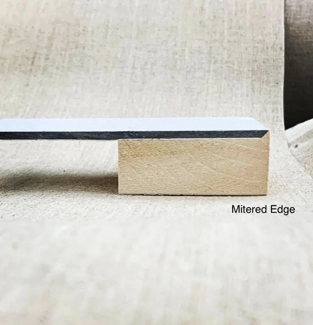 Close-up image of a mitered edge on a piece of wood, supported by a small wooden block, with the label 'Mitered Edge' in the bottom right corner.