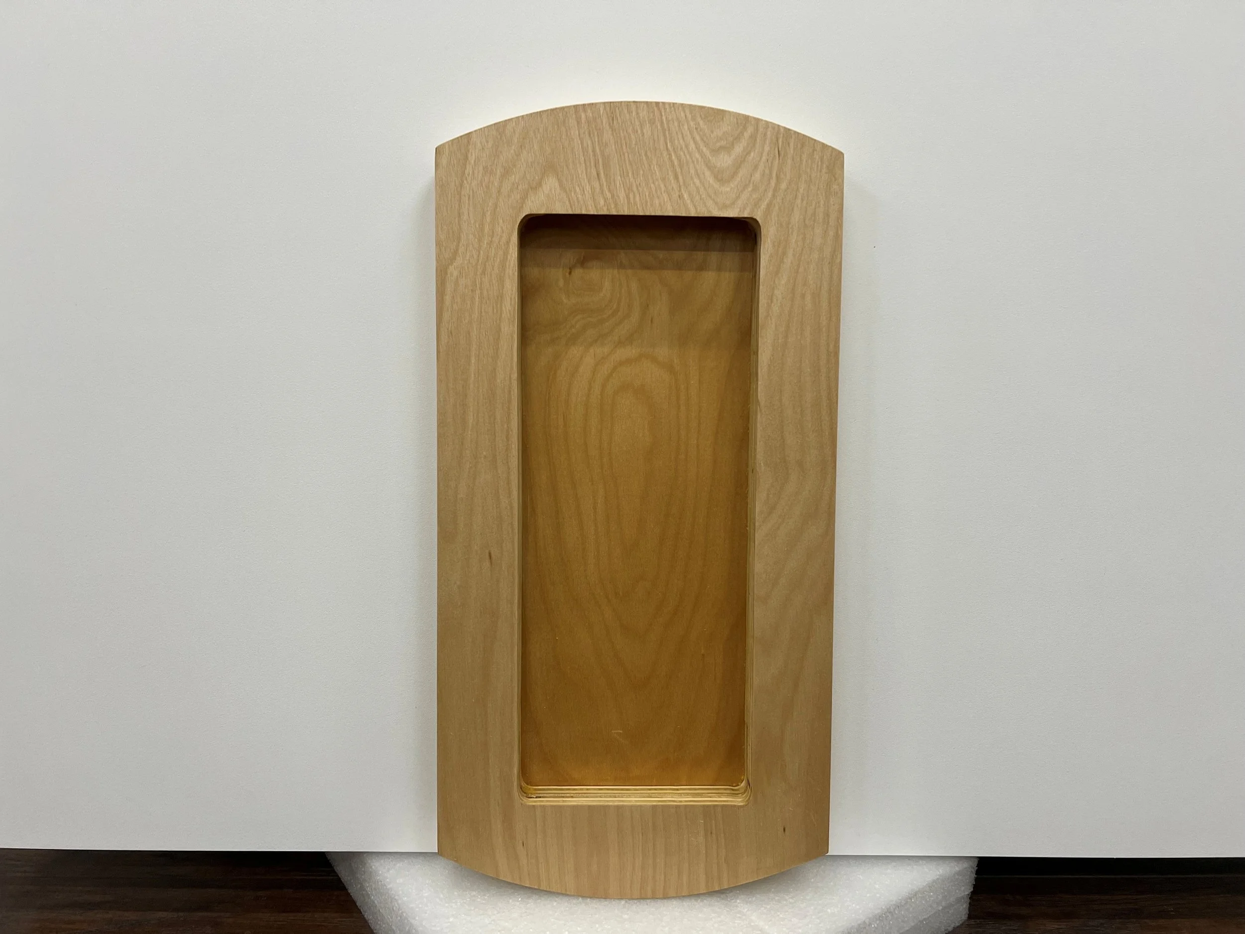A wooden rectangular shelf mounted on a white wall with an arched top and a recessed area at the bottom.