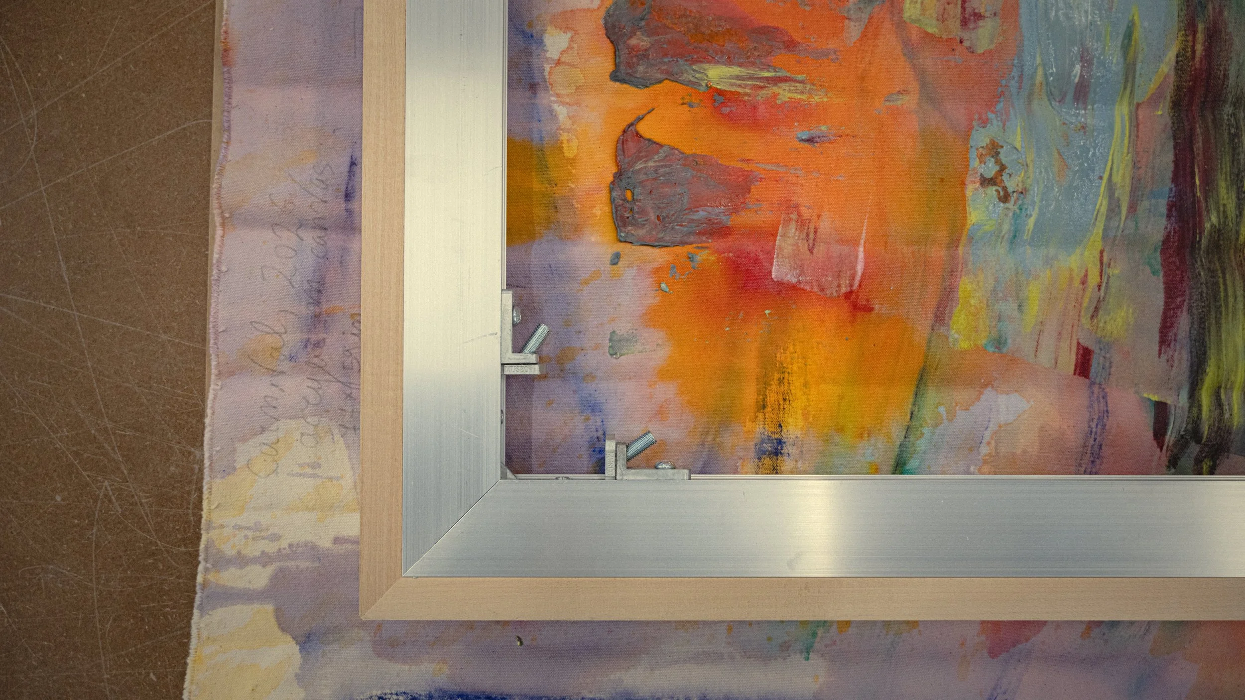 A Francine Tint art piece featuring vibrant, abstract, and textured paint strokes in shades of orange, yellow, blue, green, and gray, with an A-Liu-Minum stretcher corner on top.