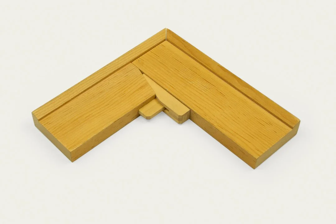 A wooden tangram puzzle piece on a white background, forming an L-shape with two rectangular sections and a small rectangular connector.