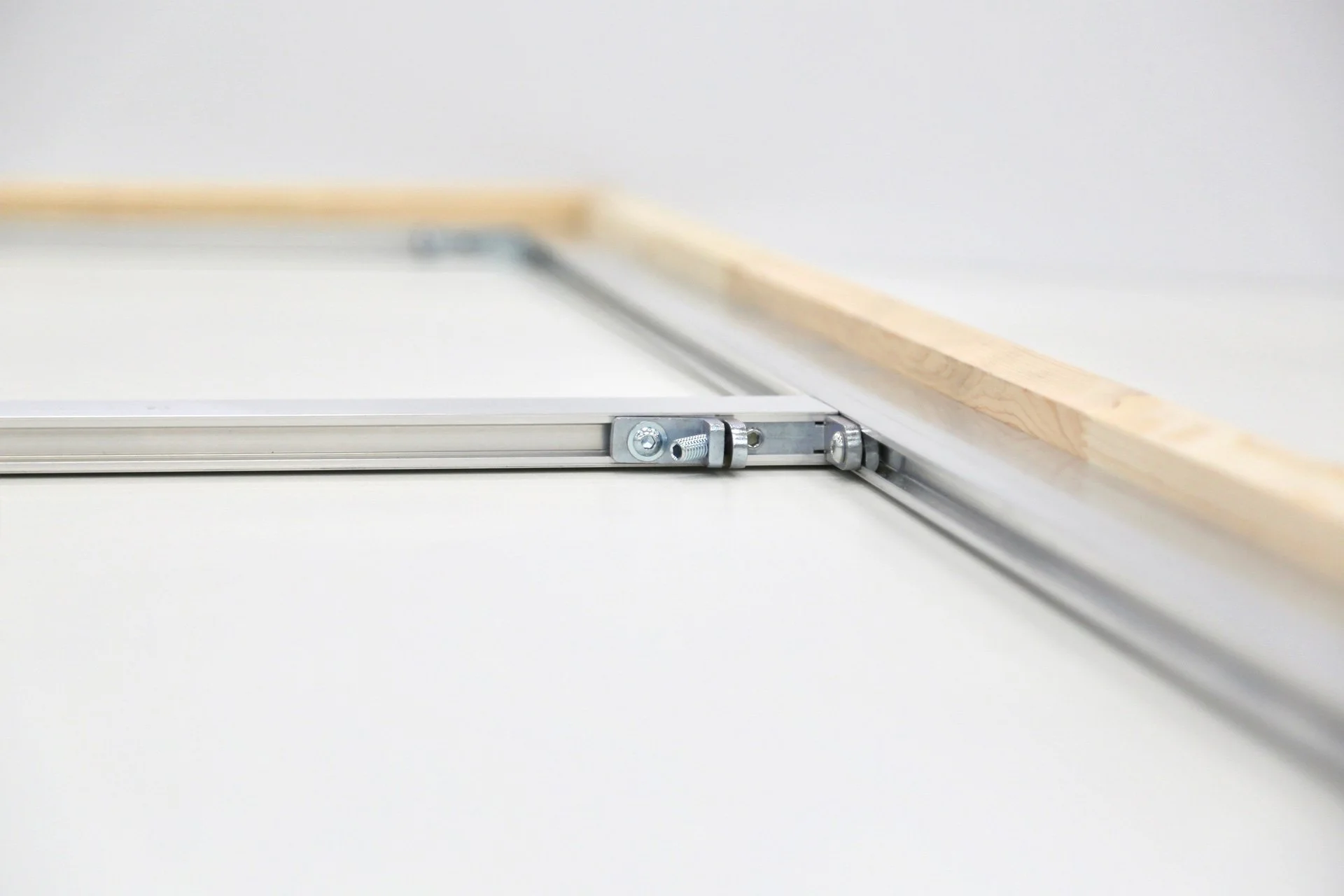 Close-up of a metal sliding mechanism with a wooden strip resting on top, on a white surface.