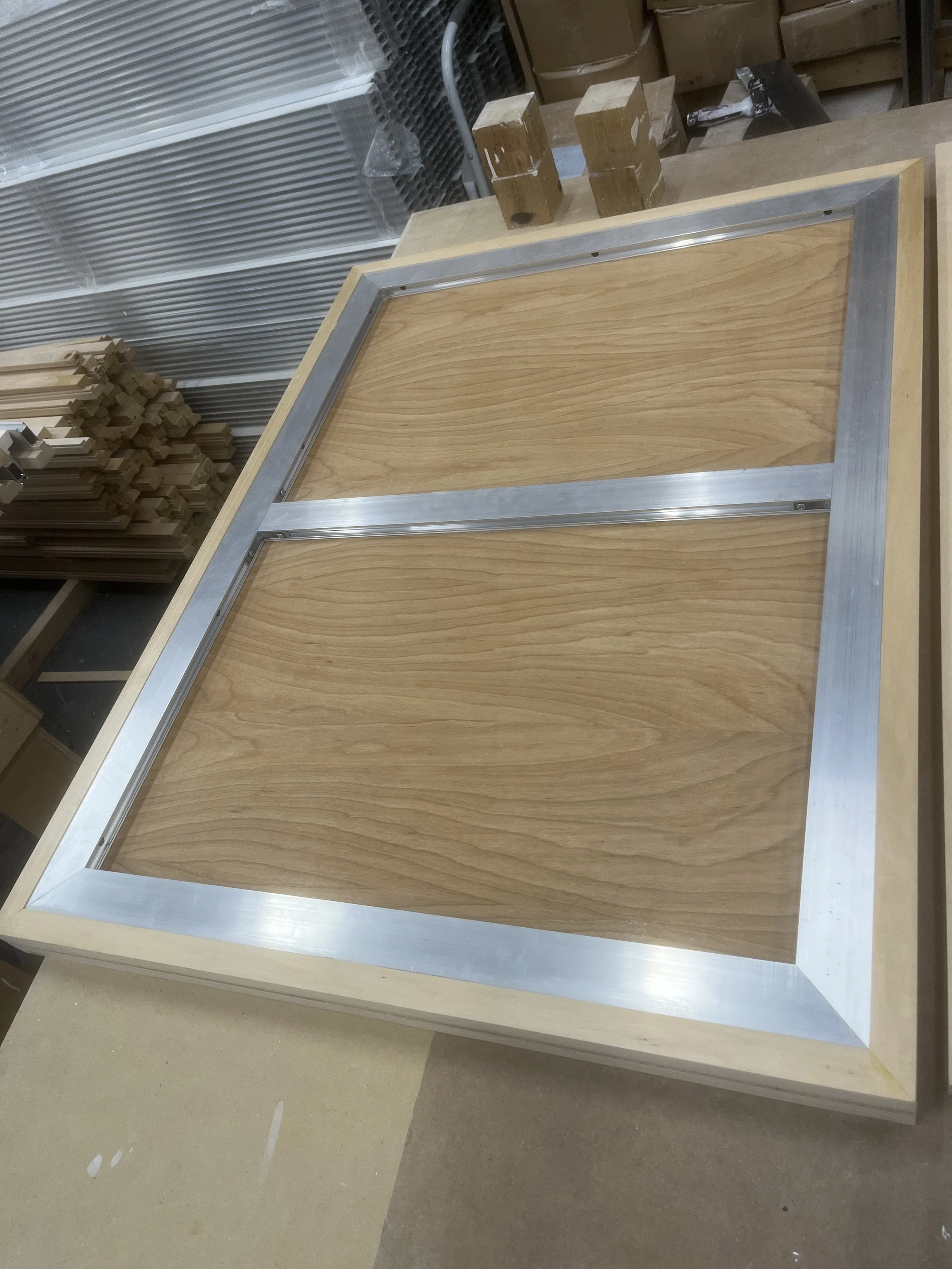 Wooden frame with metal edges placed on a workbench, with wooden blocks on top, in a workshop setting.